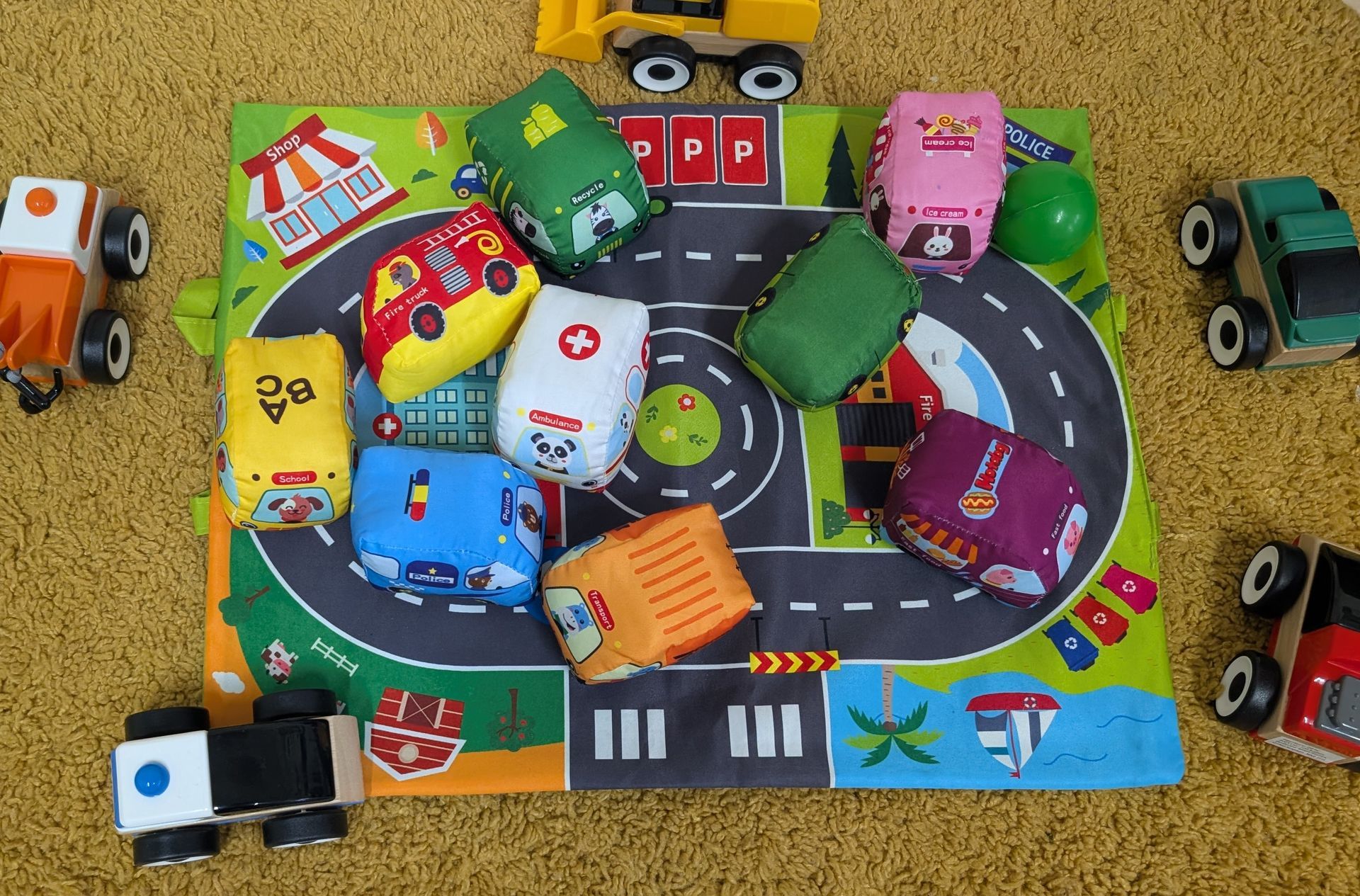 Colorful toy cars and buildings arranged around a cardboard road play scene.