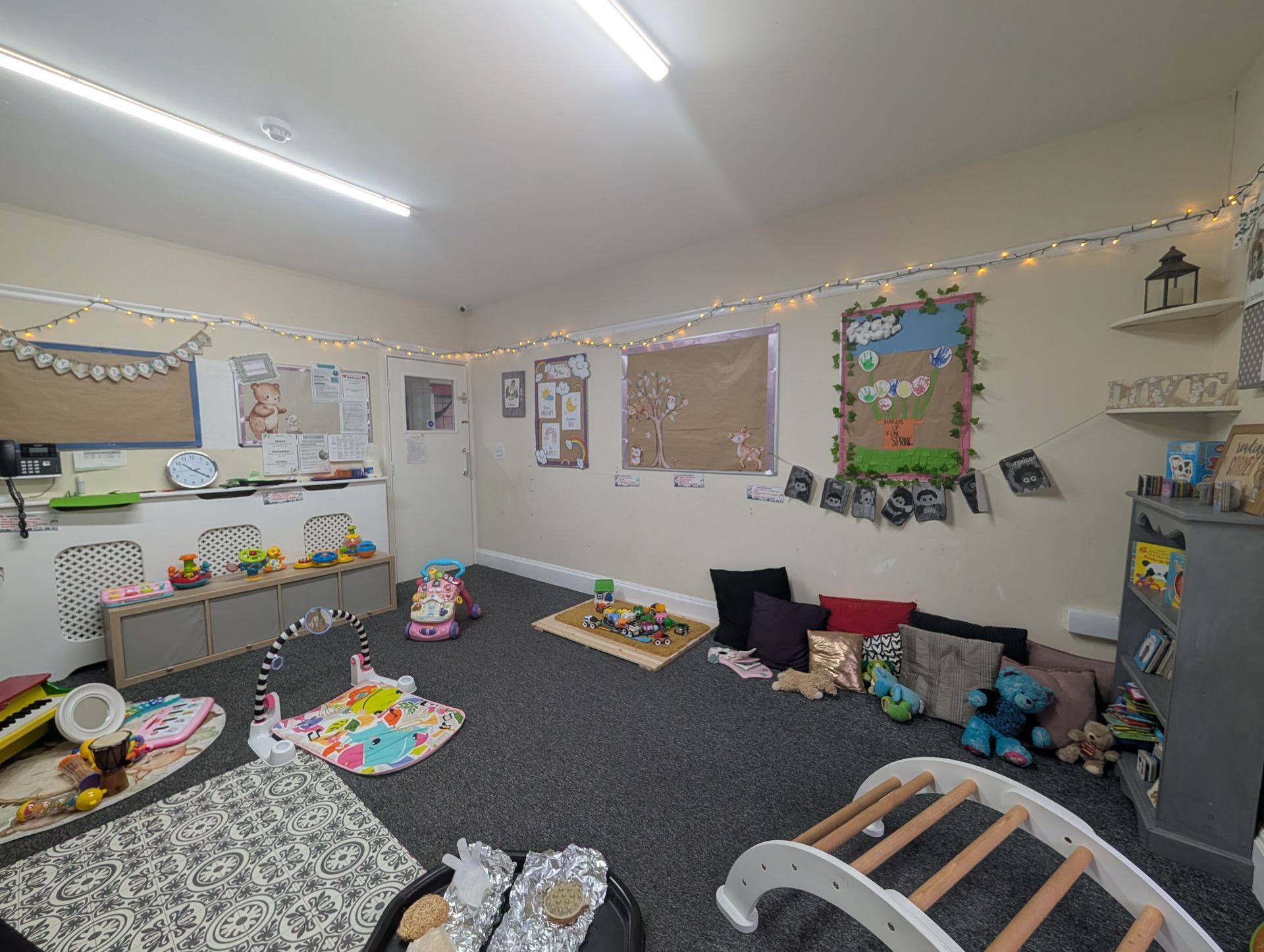 Quiet classroom with toys, rugs, wall art, string lights, and windows with blinds