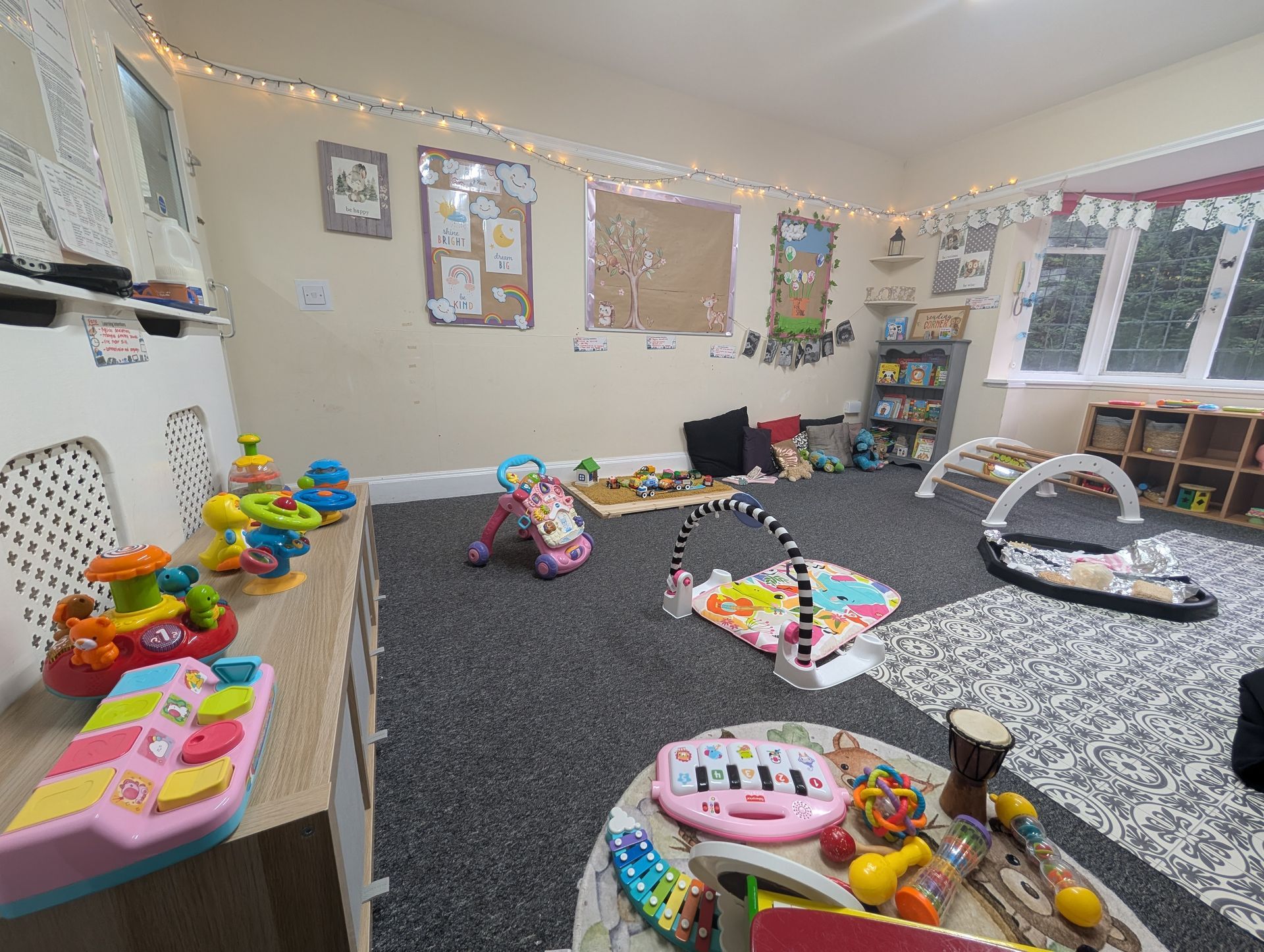 Toy-filled playroom with scattered baby toys, play mats, and colorful wall decorations.