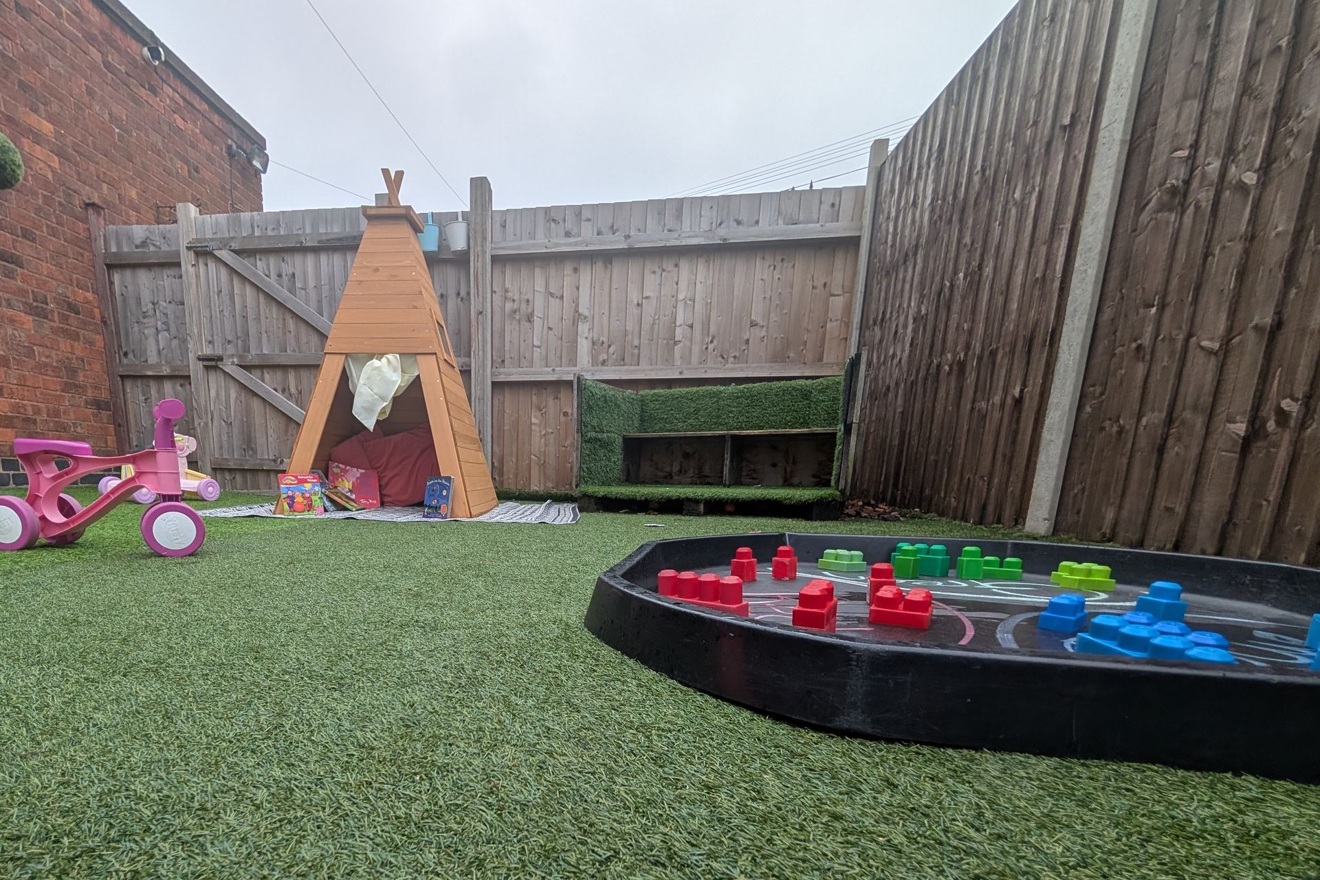 Backyard with artificial turf, a wooden play tent, toys, and a round water tray with colorful boats