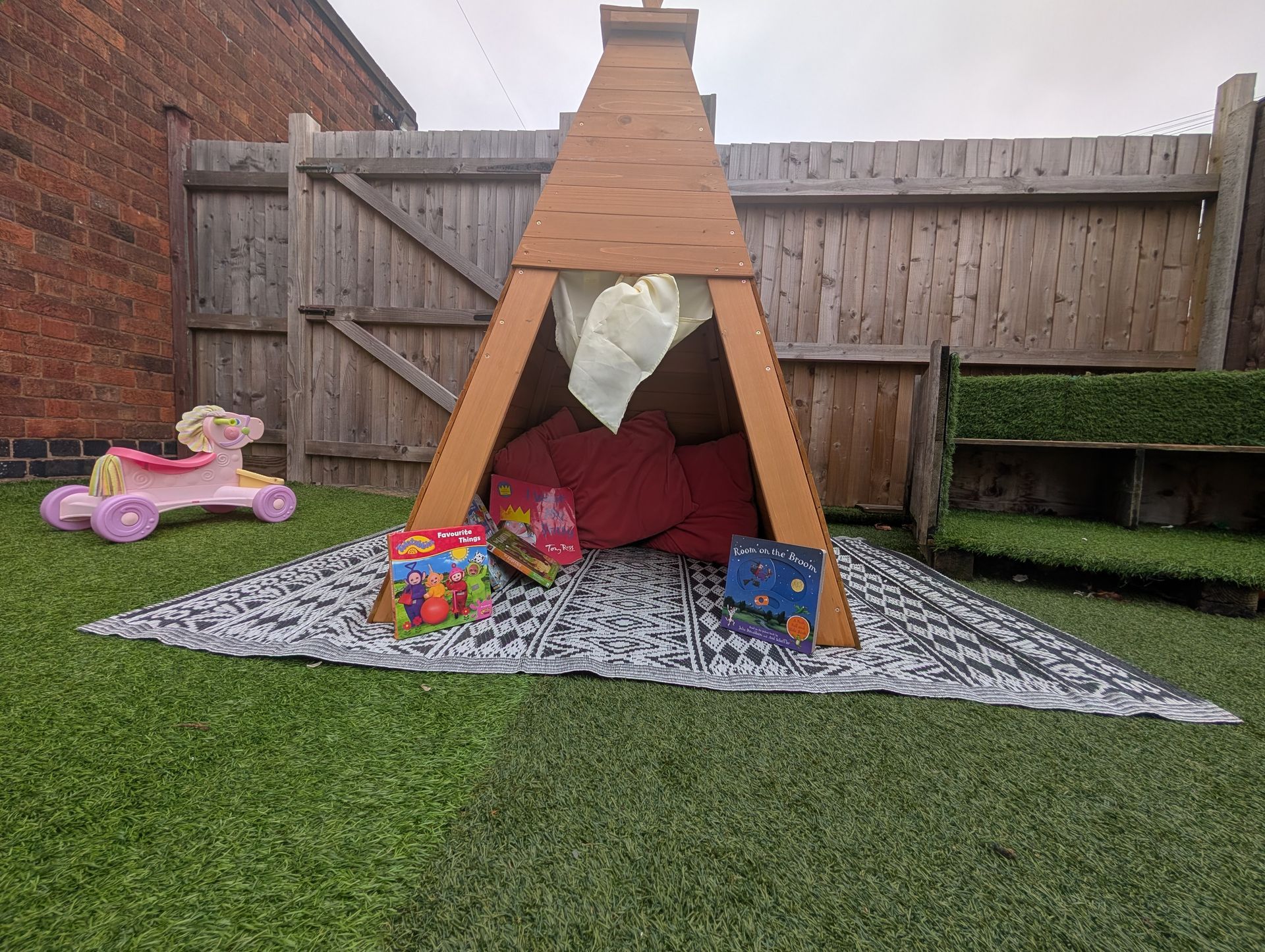 Children’s teepee play tent in a backyard on a gravel mat, with toys around it
