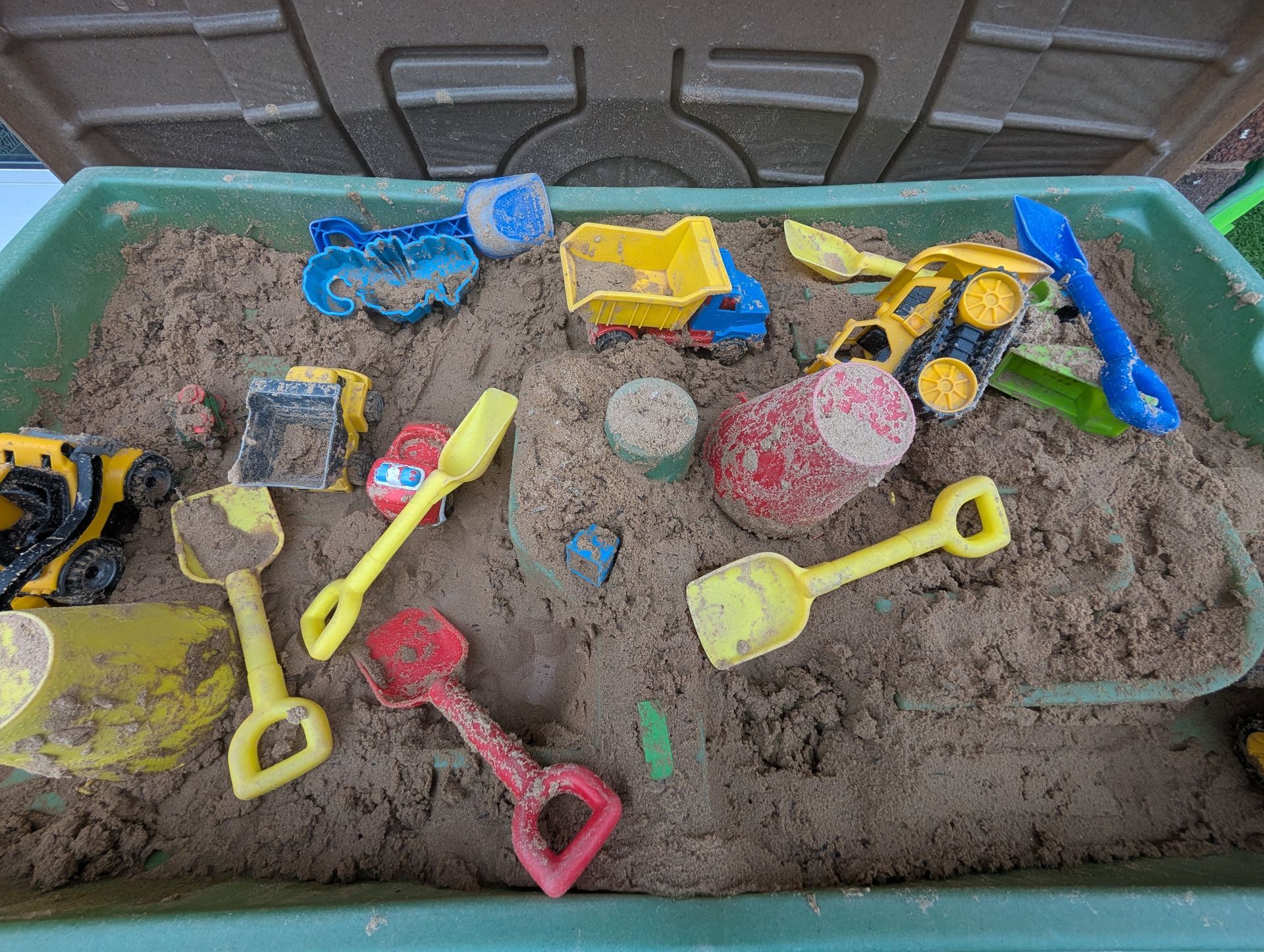 Sandbox tray with colorful toy trucks, shovels, and buckets in sand