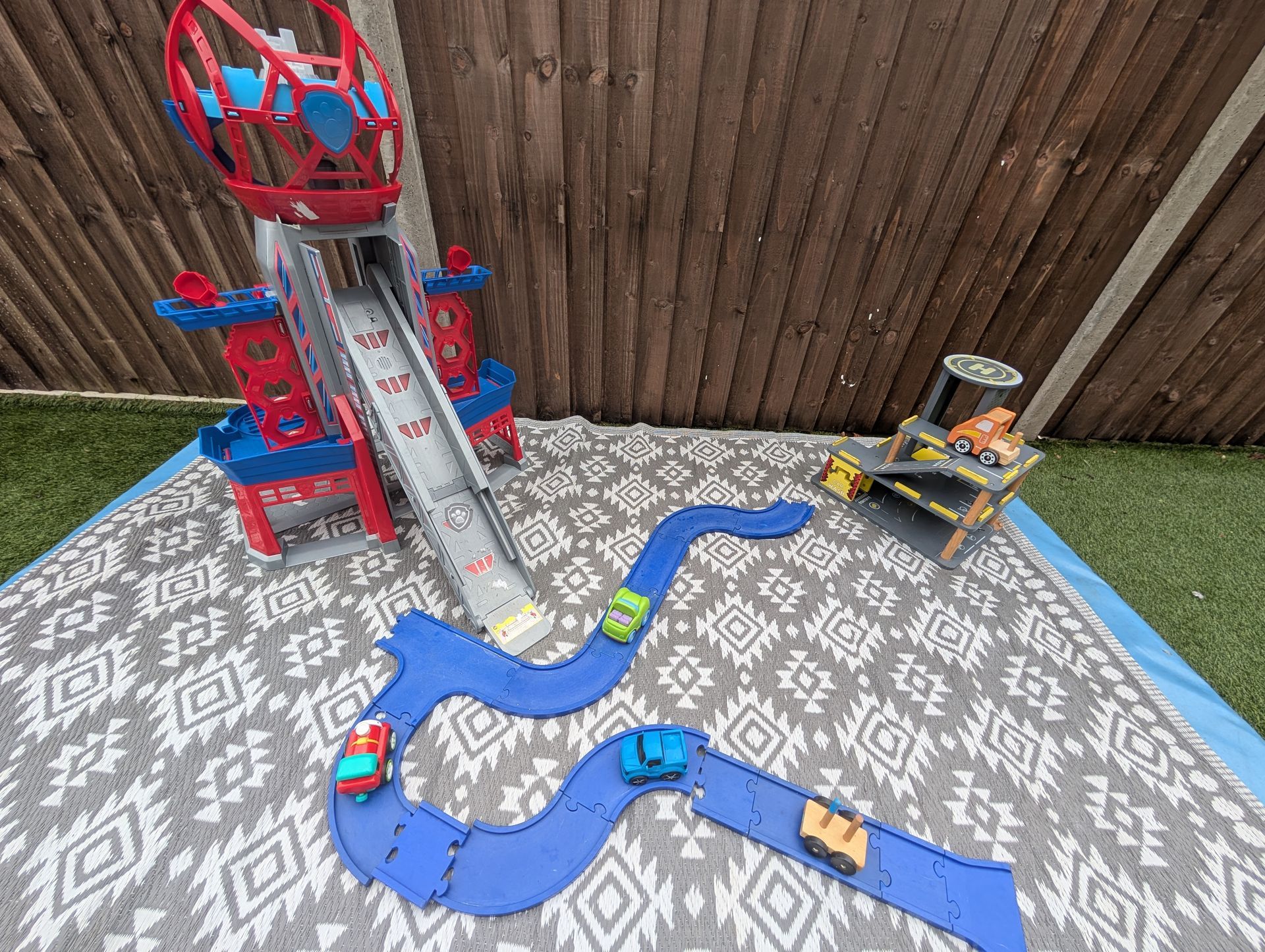 Toy race track set on a patterned rug, with a red spiral ramp, blue tracks, and toy cars.