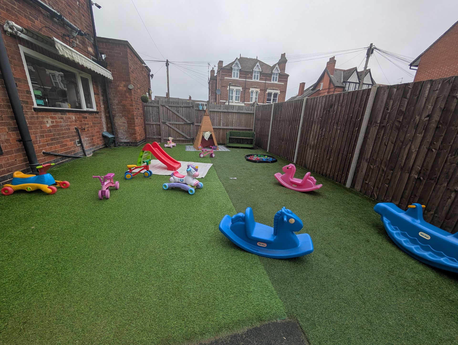 Backyard play area with colorful ride-on toys and a child near the back fence