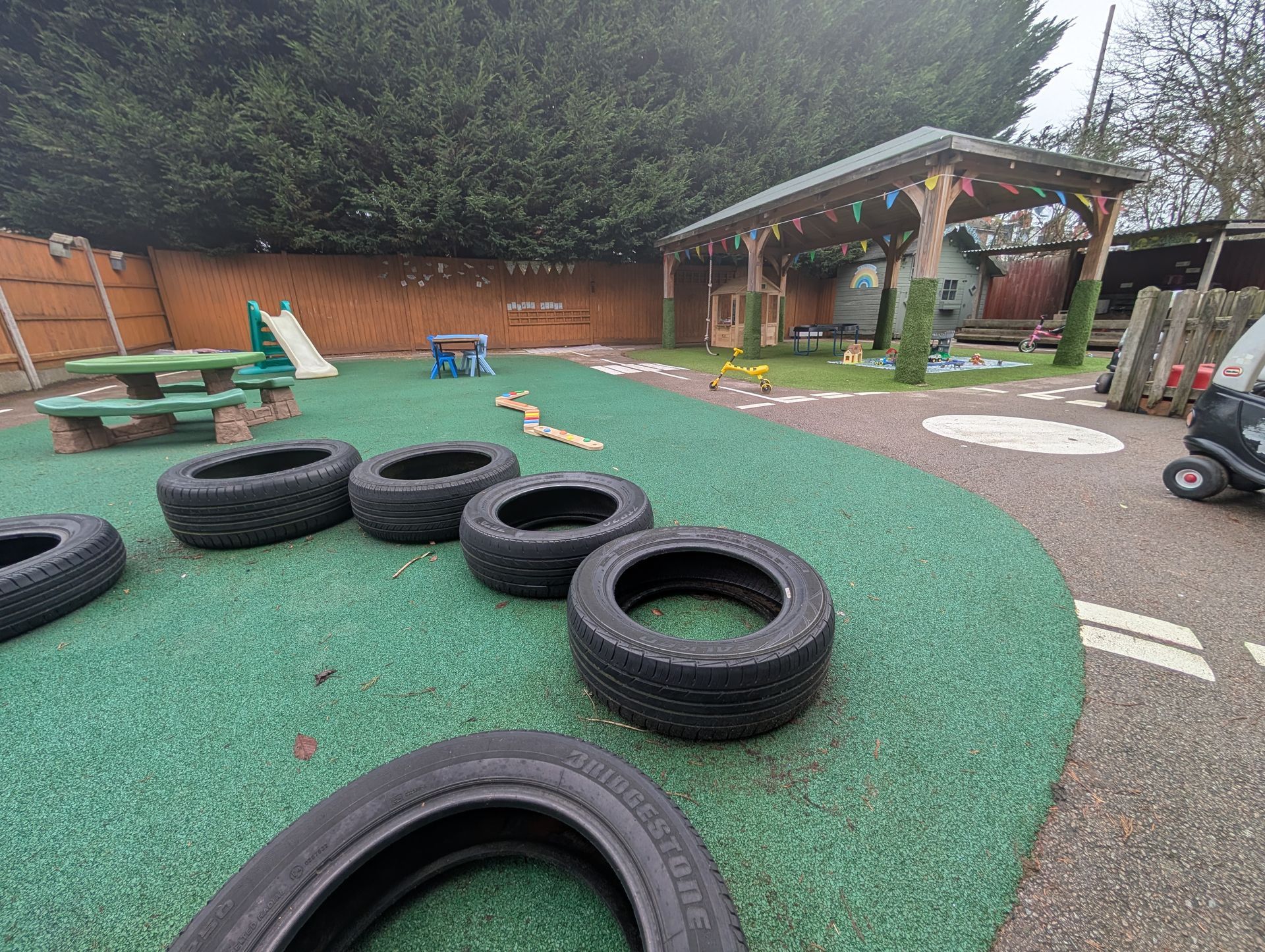Outdoor playground with green turf, tires, and a wooden shelter in the background
