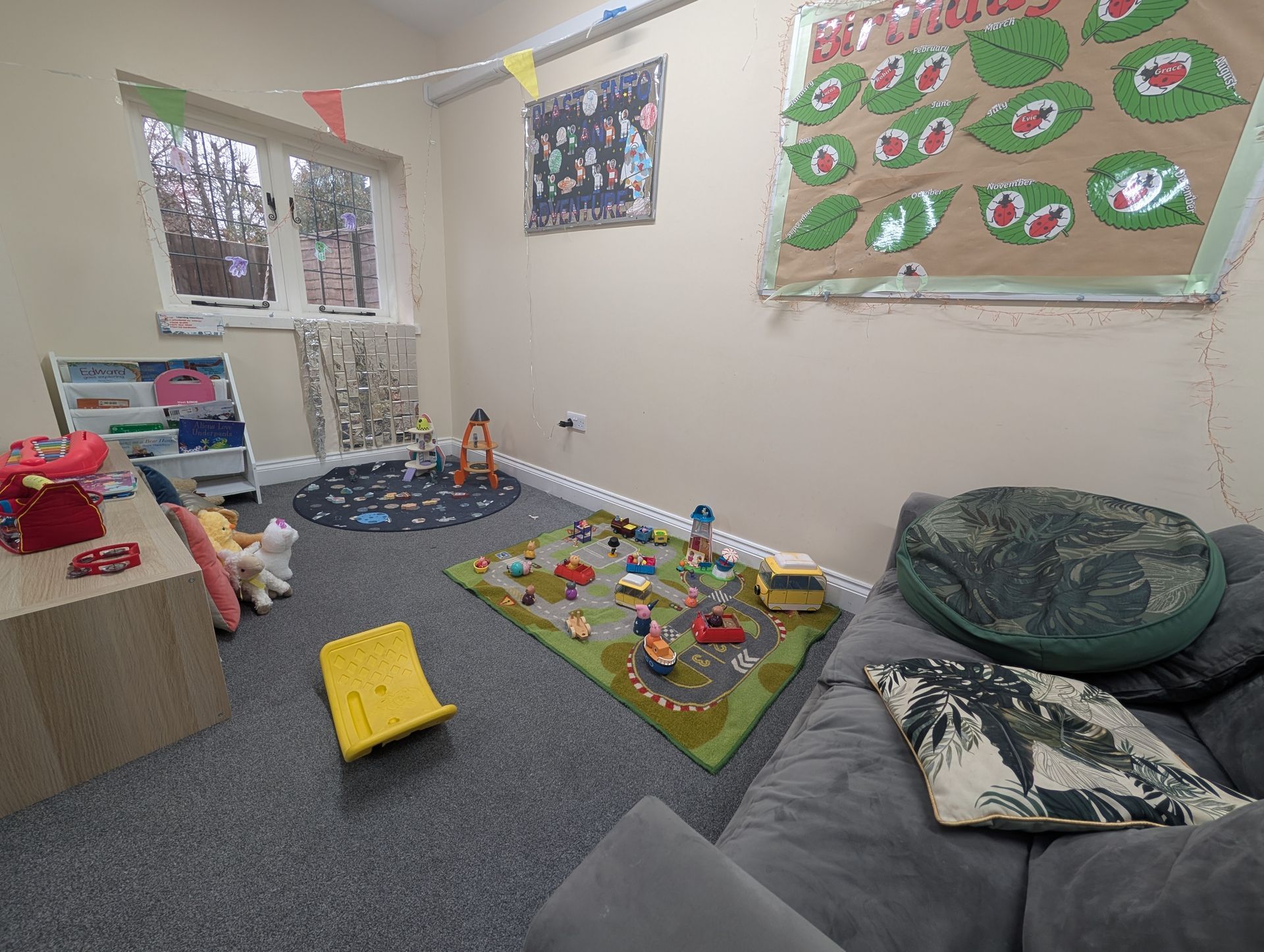 Child’s playroom with toy track, play mat, beanbag, posters, and scattered toys on a blue carpet.