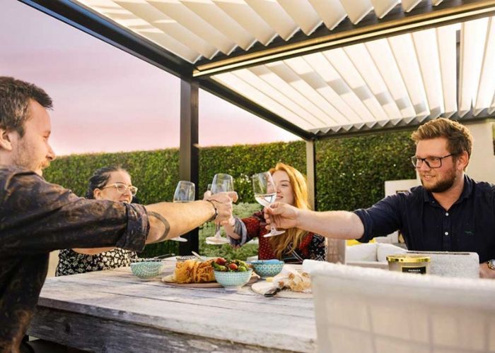 A group of people are sitting at a table toasting with wine glasses under a customised louvre