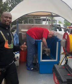 A man in a red shirt is giving a thumbs up while standing in front of a truck.