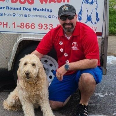 A man kneeling next to a dog in front of a dog washing trailer