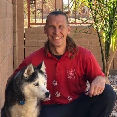 A man in a red shirt is kneeling down next to a husky dog.