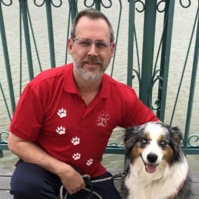 A man in a red shirt is kneeling down next to a dog.