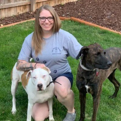 A woman is kneeling down with two dogs in the grass.