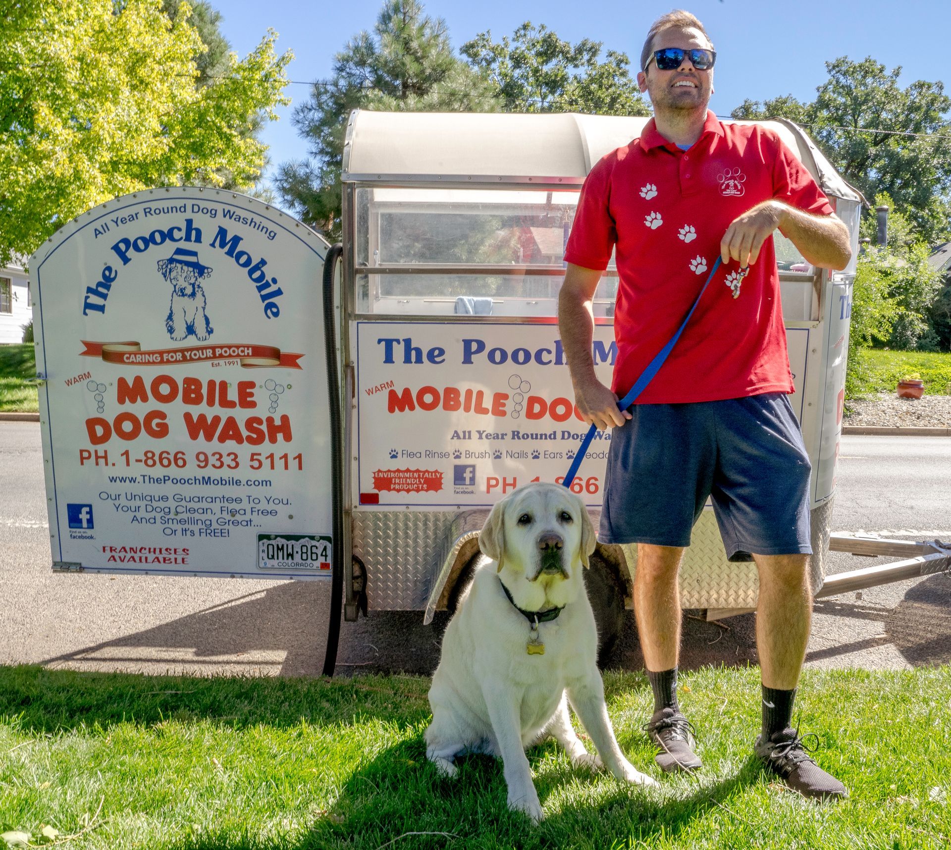 A man standing next to a dog in front of a mobile dog wash