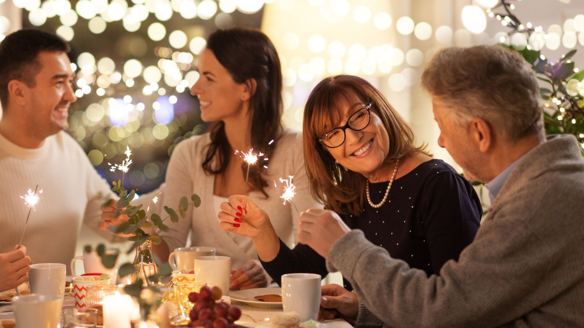 Amigos charlando en una mesa a la luz de las velas con guirnaldas de luces cálidas de fondo.