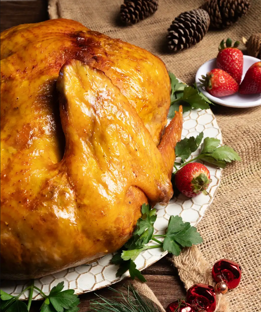 Pavo asado glaseado en una fuente con fresas y hierbas sobre un mantel de arpillera.