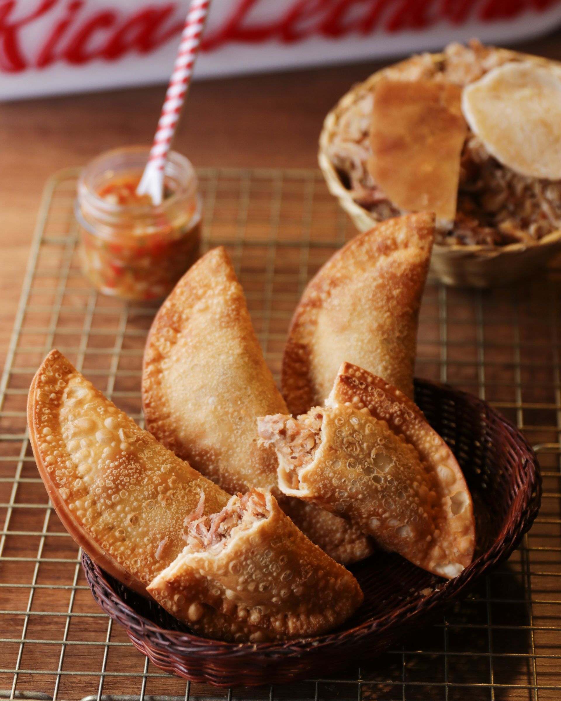 empanadas fritas en un plato con un pequeño tarro de salsa para mojar sobre un mantel individual tejido.