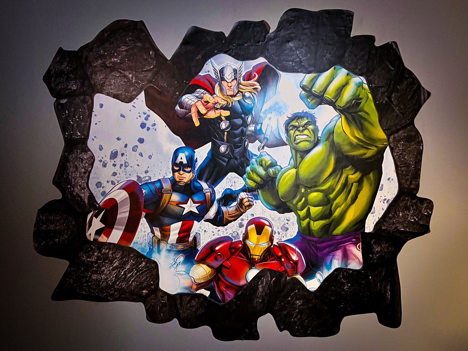 Marvel superheroes bursting through a cracked wall, including Hulk, Thor, Captain America, and Iron Man.