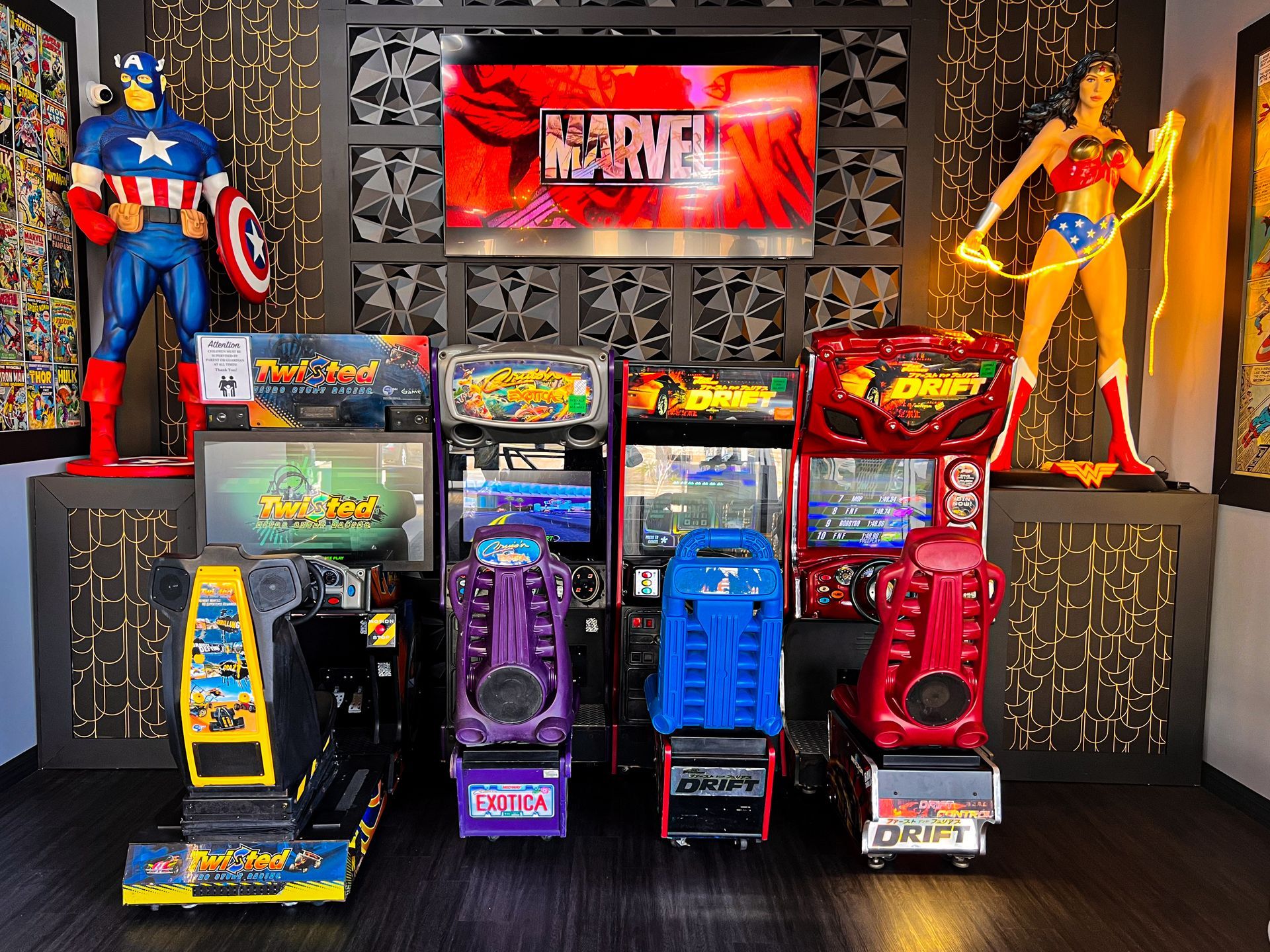 Colorful arcade game cabinets and superhero statues displayed in a themed arcade room