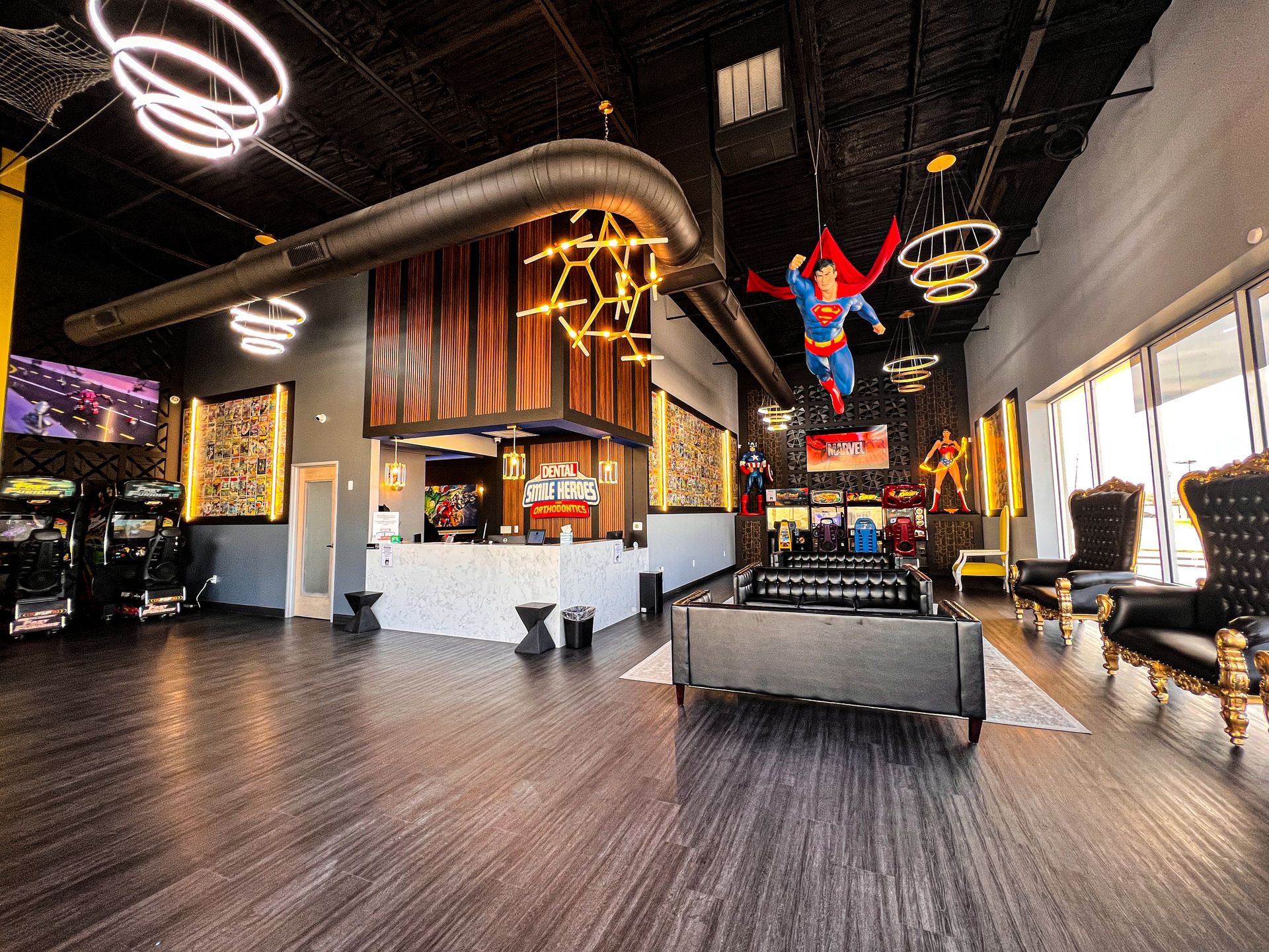 Modern indoor play lounge with black ceiling, wood floors, neon lights, and a Spider-Man figure hanging overhead