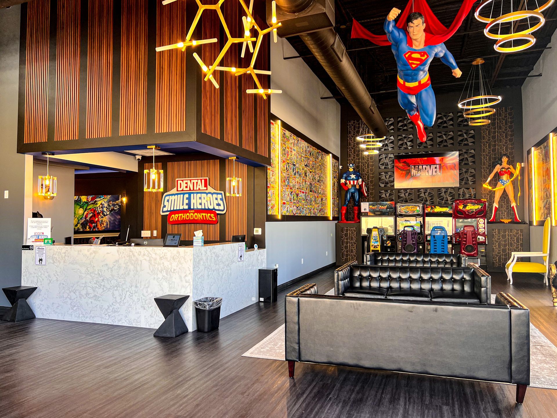 Modern lounge with Superman decor, neon lights, black couches, and a bar area in the background
