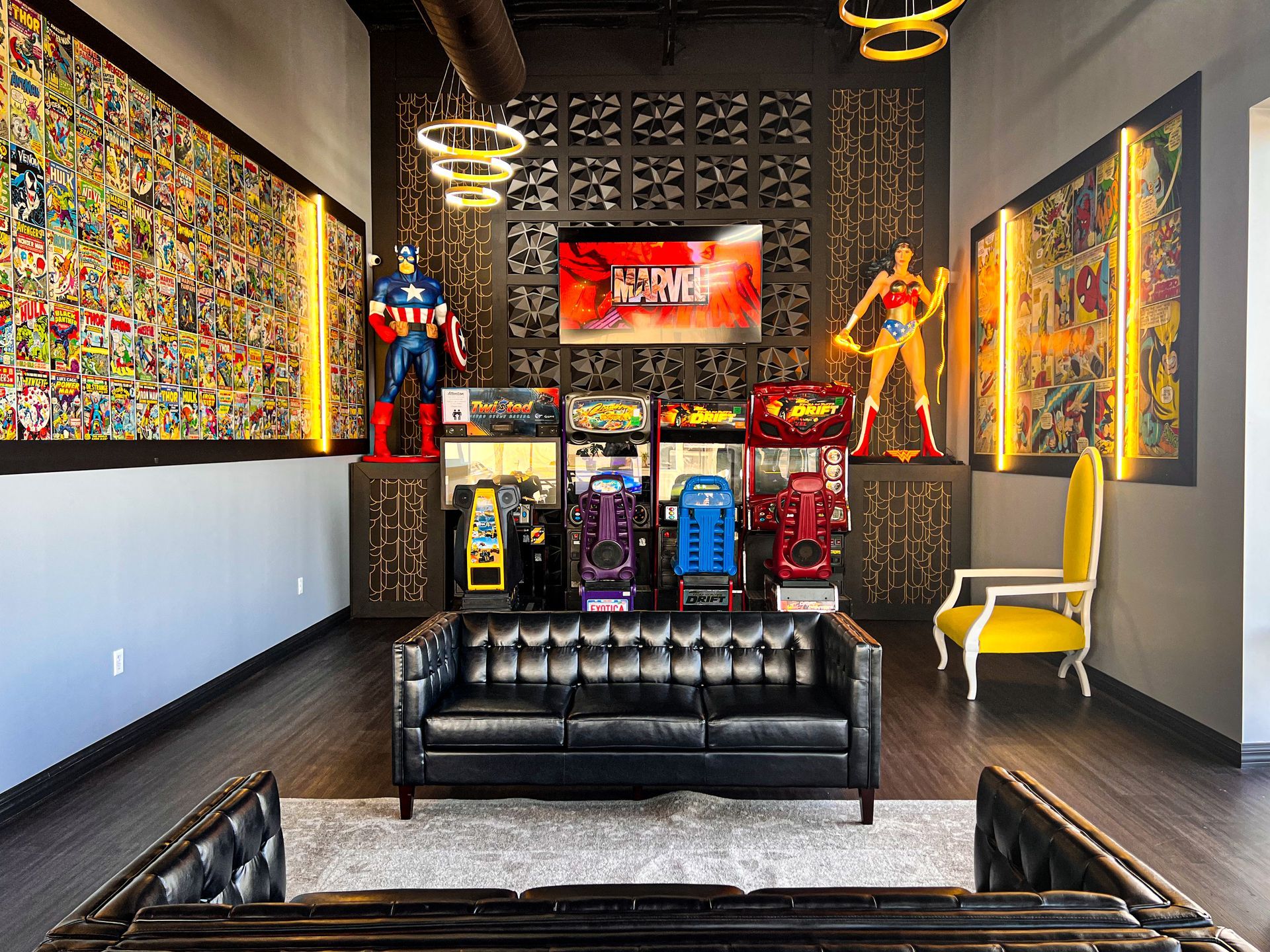 Colorful pop-art game room with arcade cabinets, superhero statues, black leather seating, and bright wall art