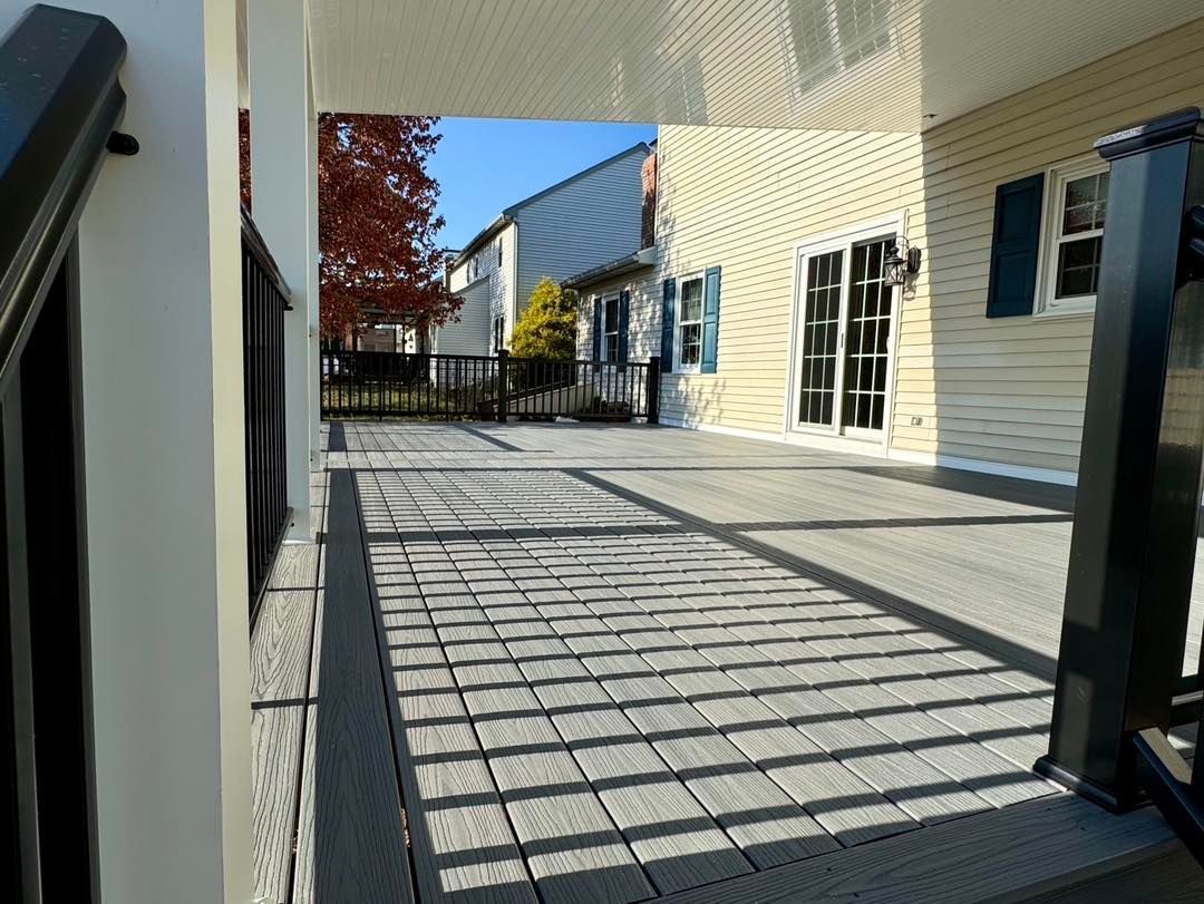 A view from a deck with grey composite flooring and dark railing, looking toward a house exterior with a sliding door.