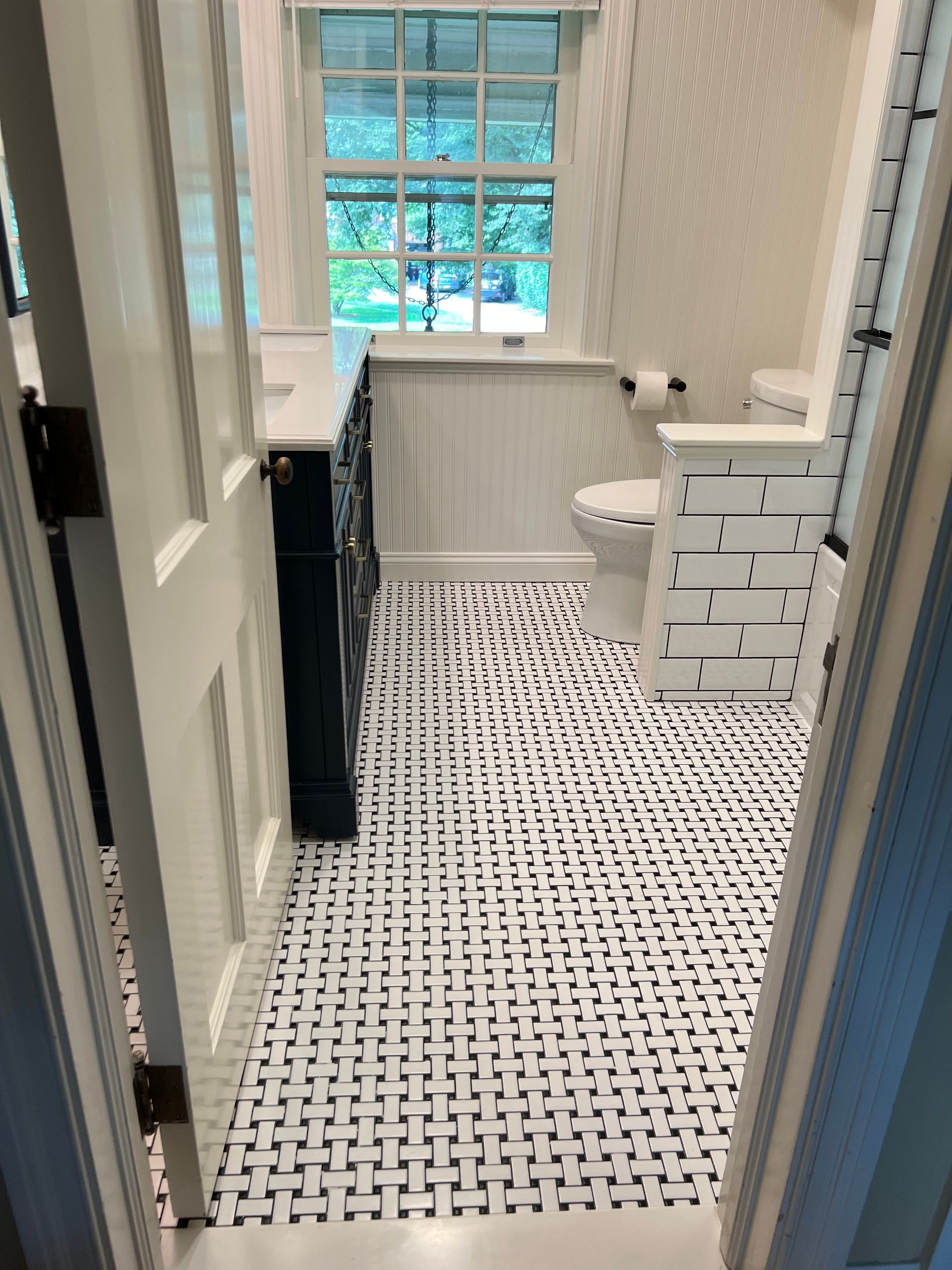 A bathroom viewed through a doorway, featuring black and white patterned tile floors, a white toilet, and a vanity.