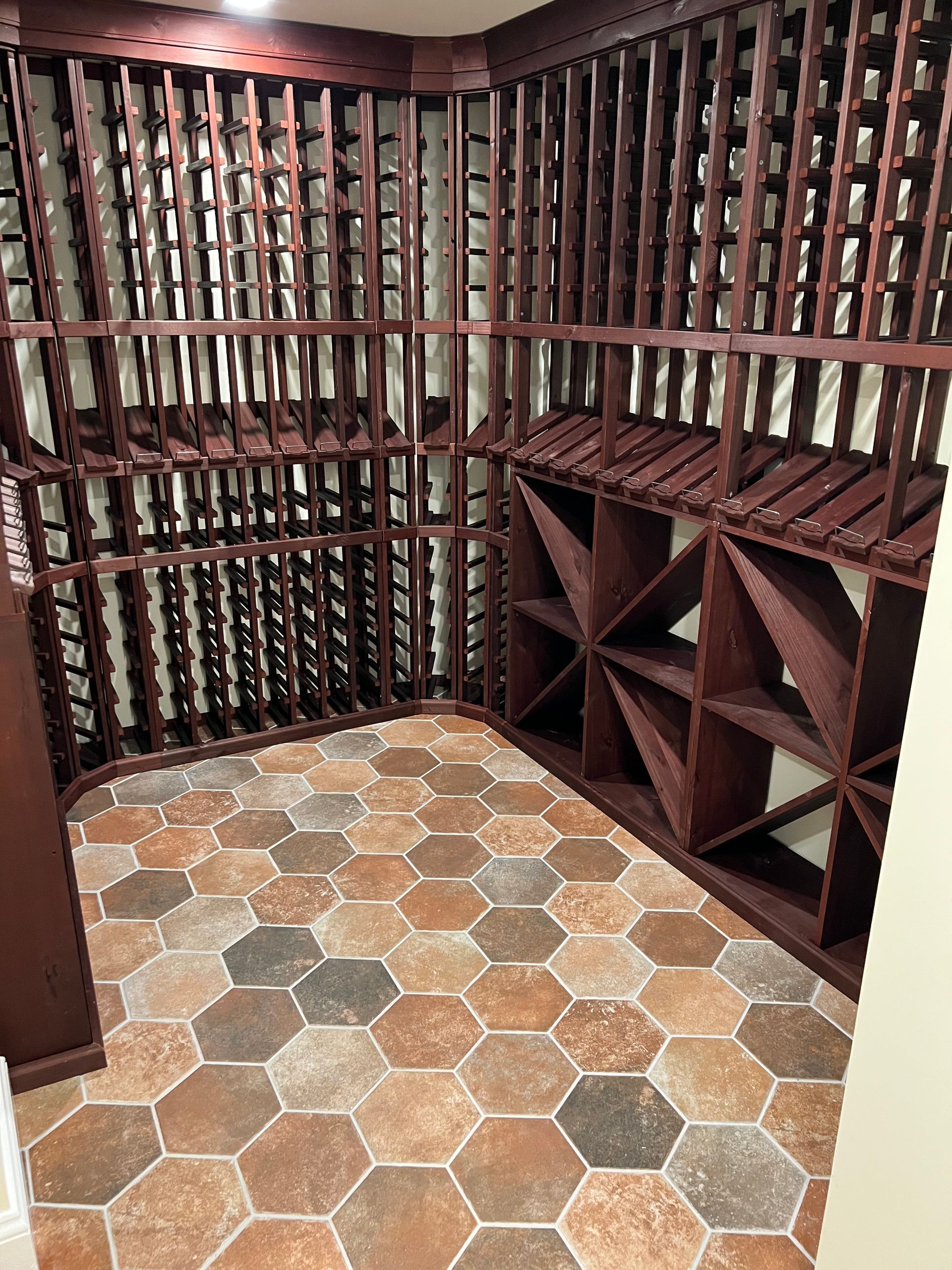 A wine cellar with dark wood storage racks, individual bottle slots, diamond-shaped bins, and hexagonal tile flooring.