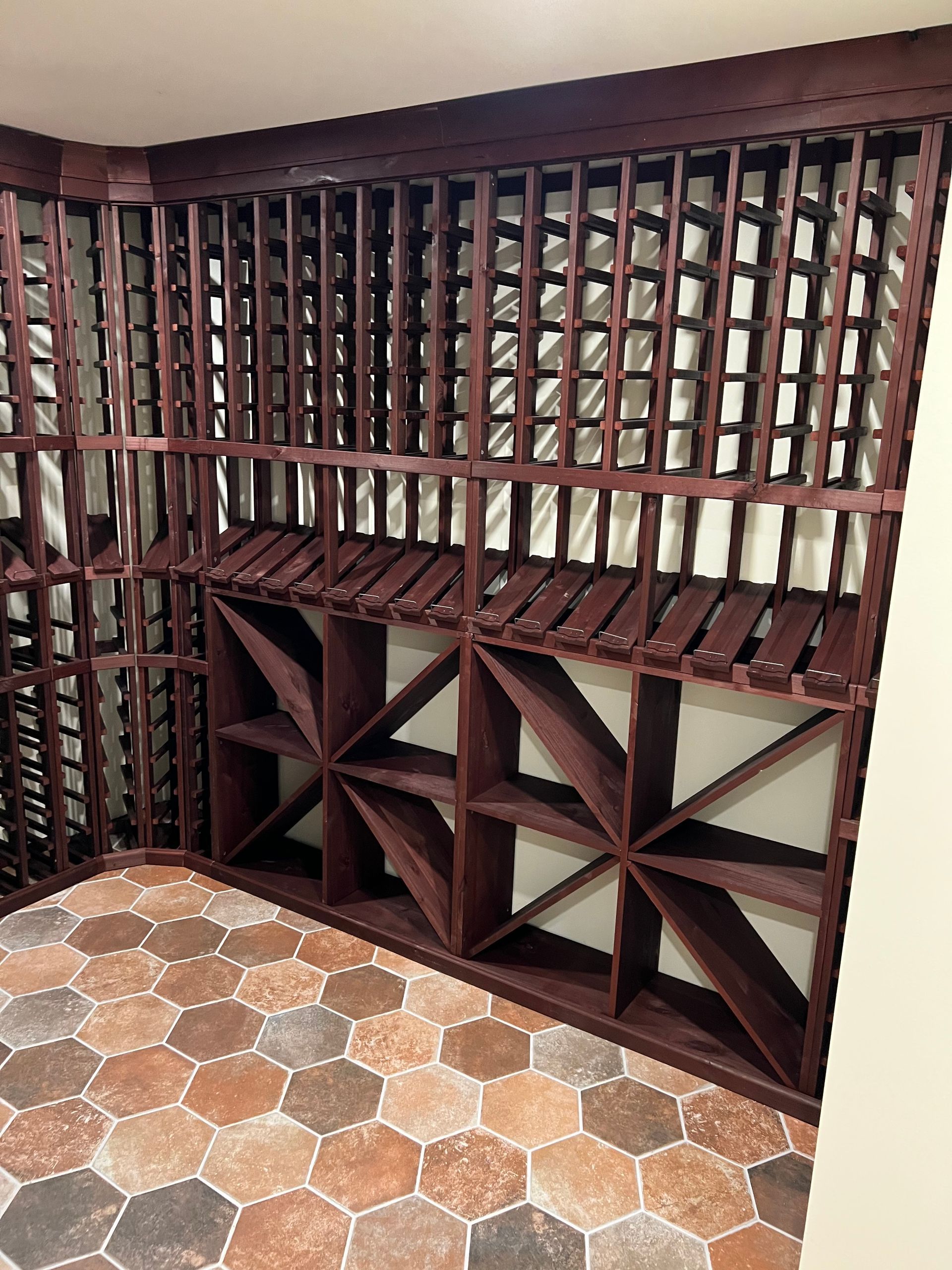 Custom dark wood wine racks with diamond-shaped storage and individual bottle slots in a room with hexagon tile flooring.