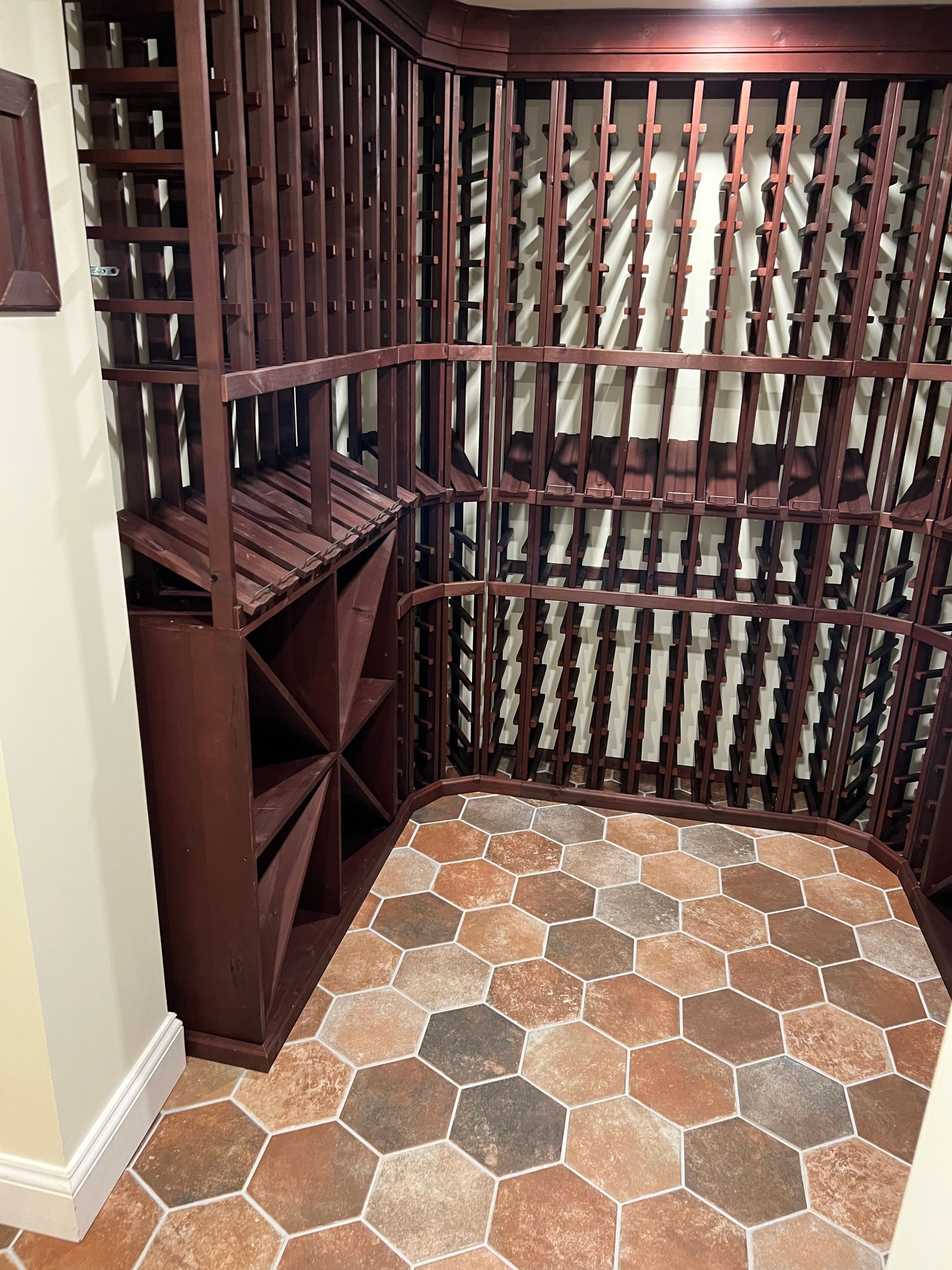 A corner wine cellar with dark wood storage racks and hexagonal, multi-toned stone floor tiles.