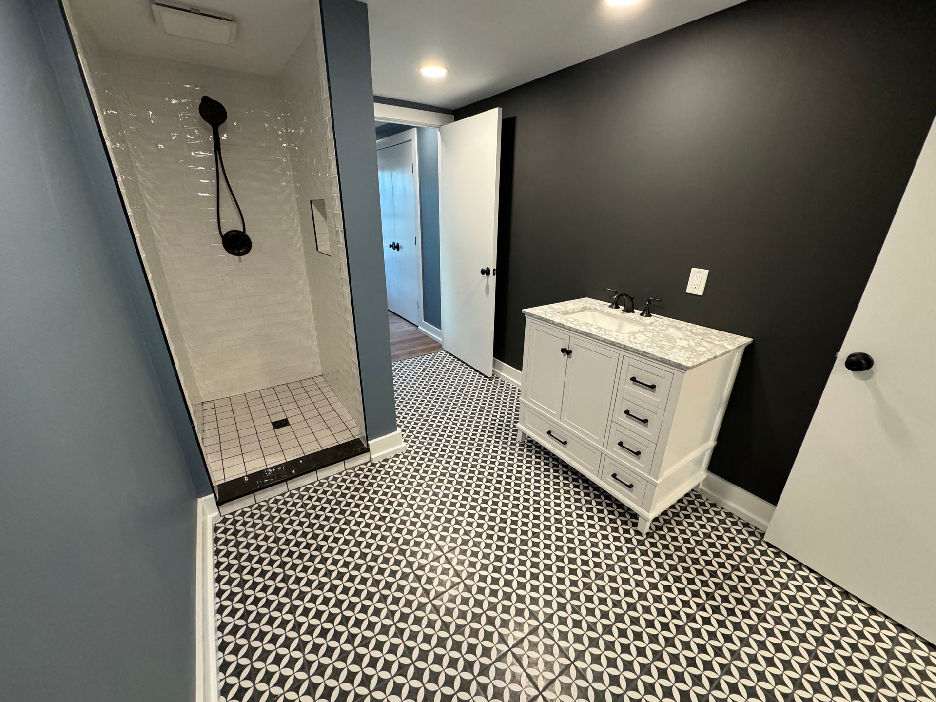 A modern bathroom with black and white patterned tile flooring, a shower with white subway tiles, and a white vanity.