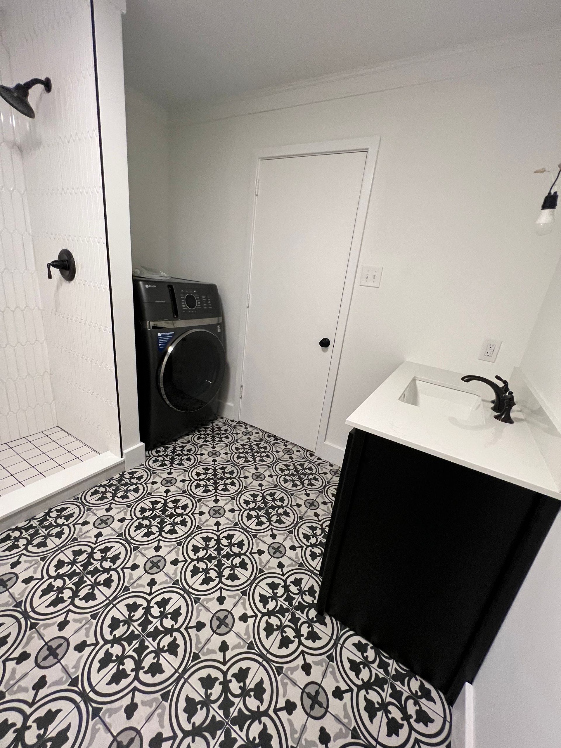 A modern bathroom featuring patterned black and white floor tiles, a black washing machine, and a vanity with a white top.