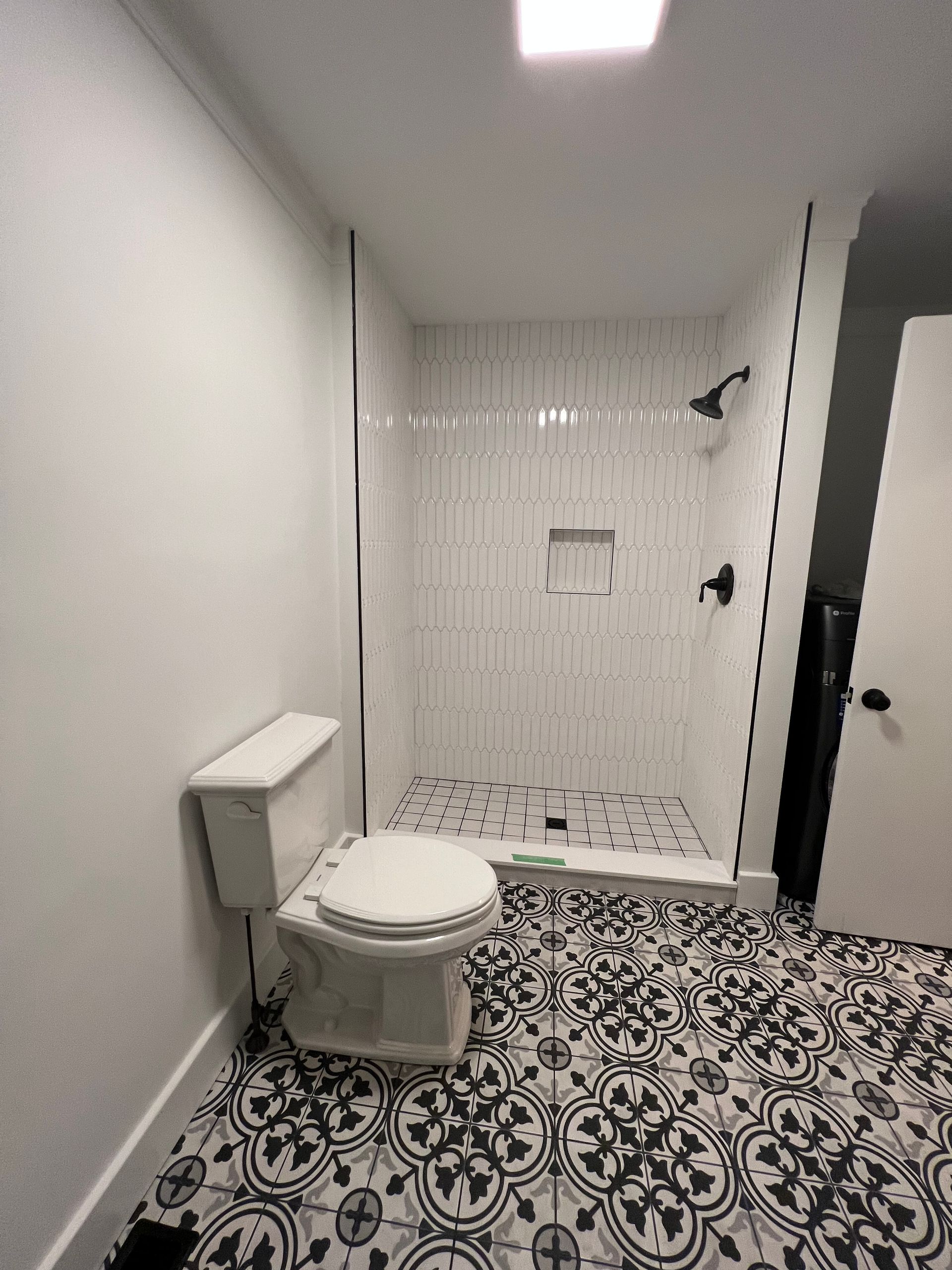 A bathroom with a toilet, black-and-white patterned tile flooring, and a walk-in shower with white vertical wall tiles.