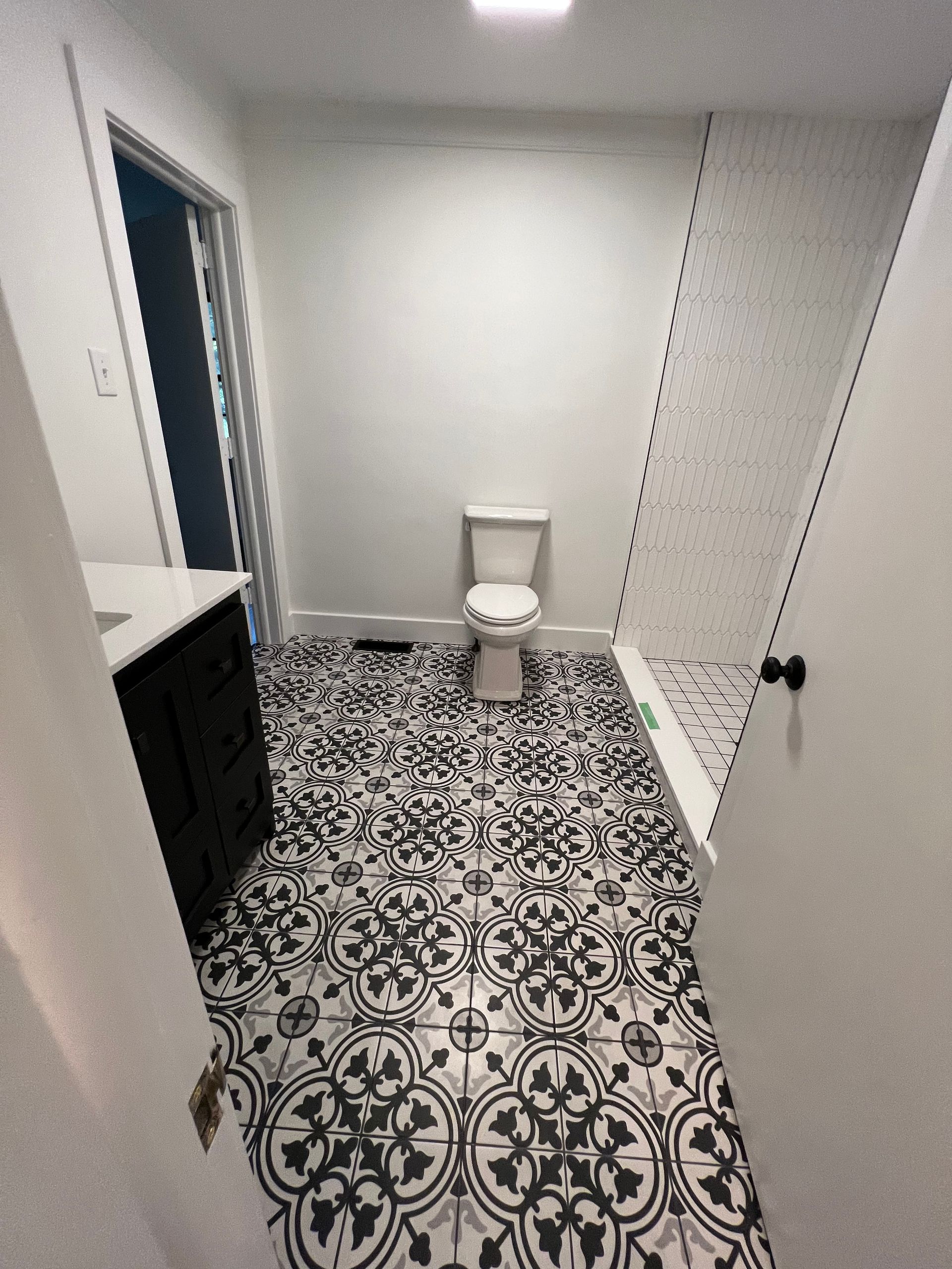 A bright bathroom with black-and-white patterned floor tiles, a black vanity, a white toilet, and a tiled shower stall.