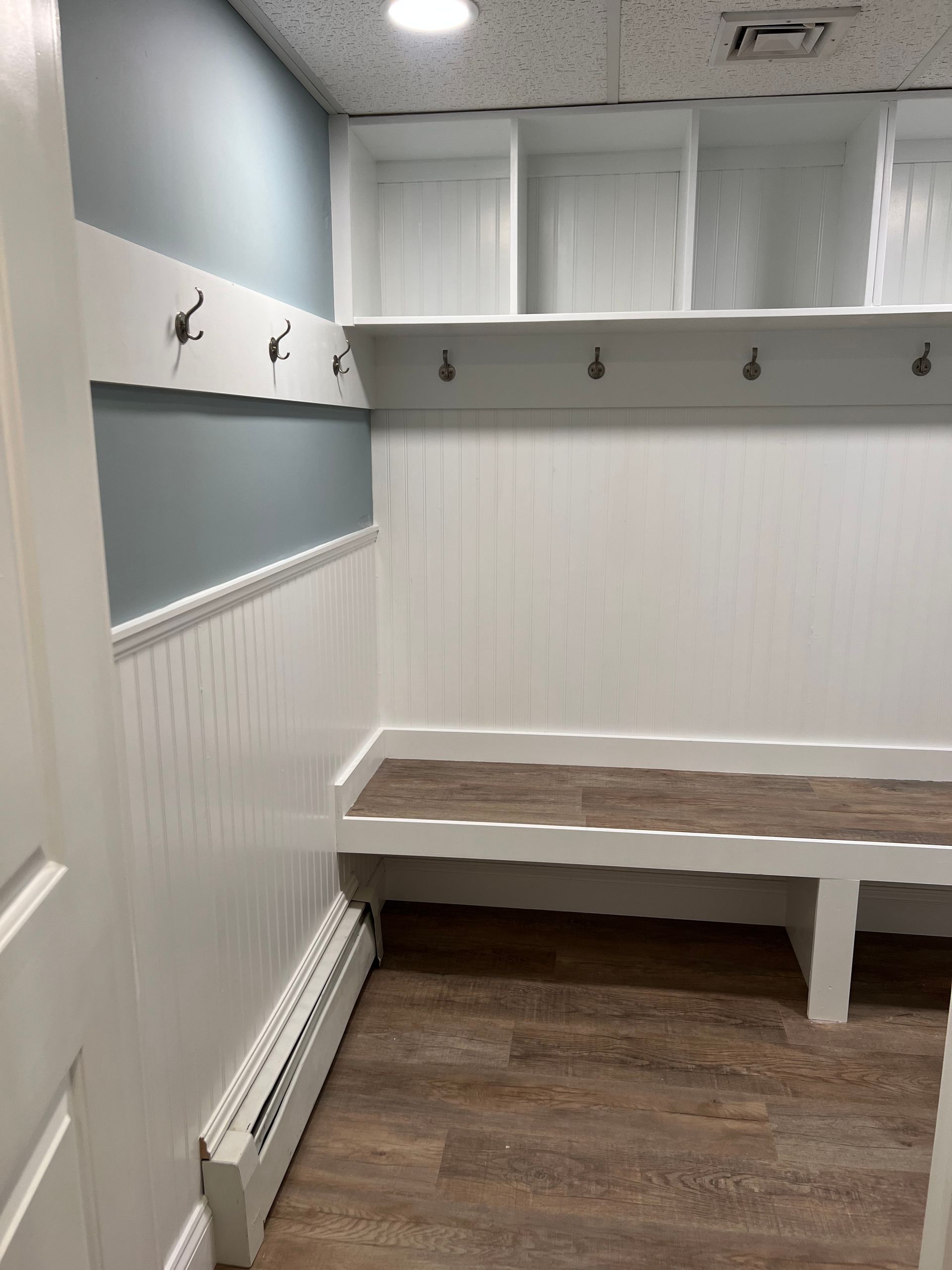 A mudroom featuring white built-in storage cubbies, coat hooks on a blue wall, white wainscoting, and a wooden bench seat.