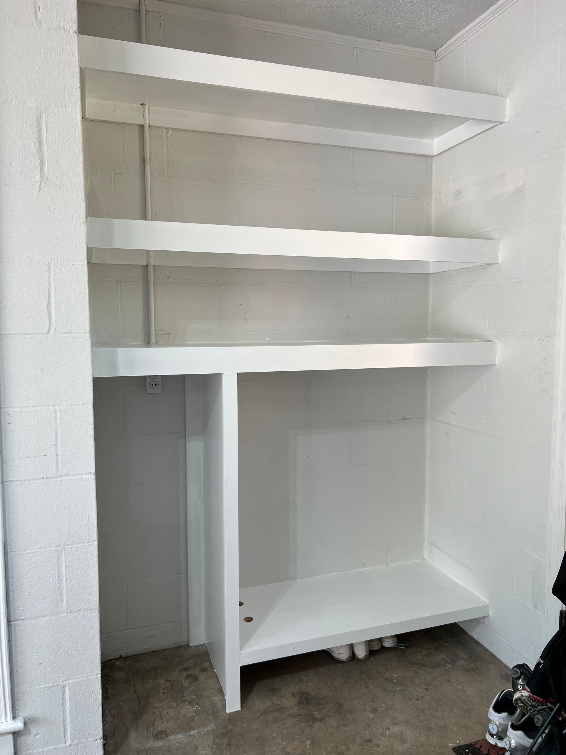 A white, multi-tiered wooden shelving unit built into a recessed wall area with concrete floors.