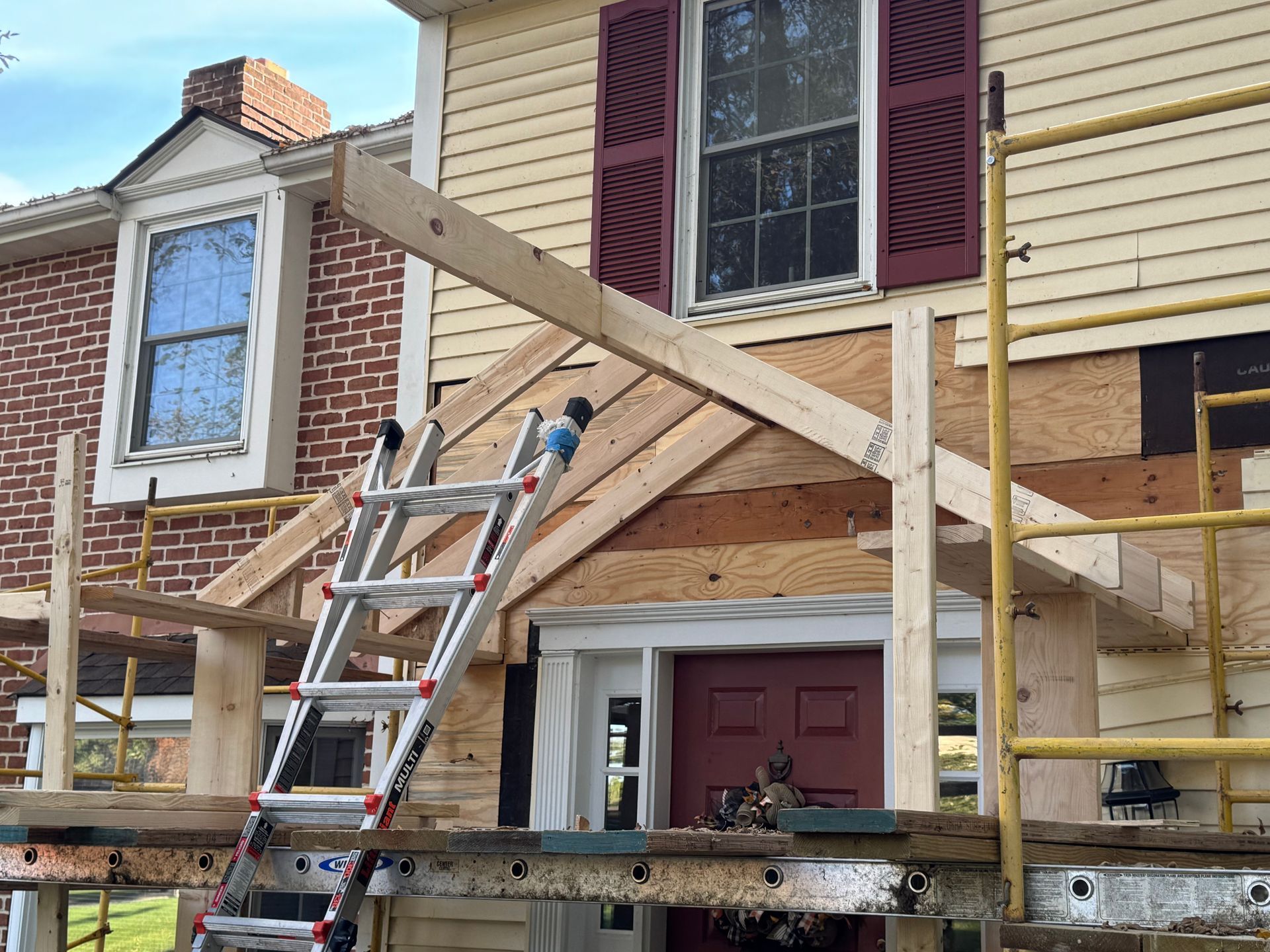 Construction scaffolding surrounds the entrance of a house, where a new wooden porch frame is being built.