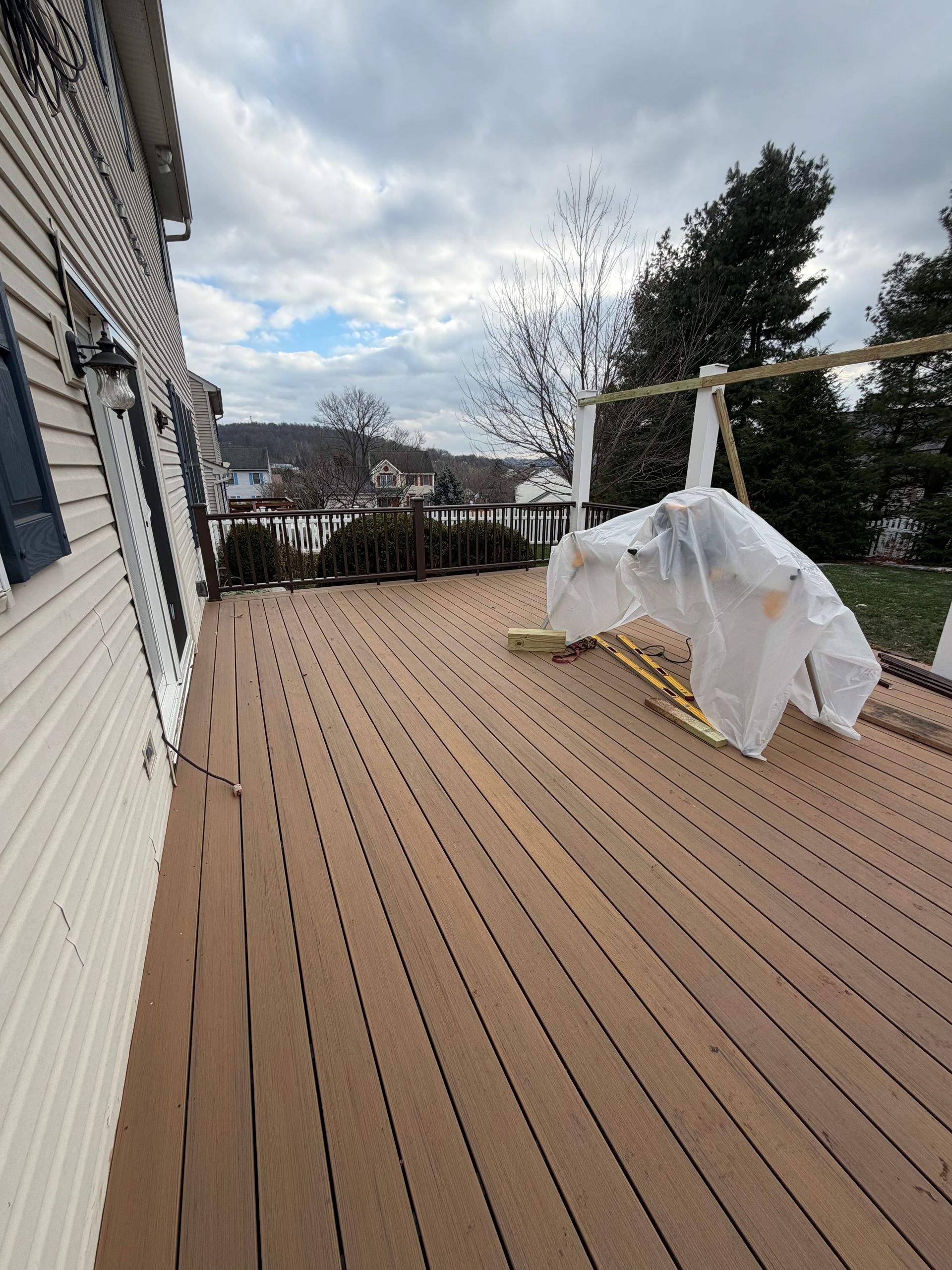 A spacious wooden deck extending from a house, with a covered structure and an open view of hills and trees.