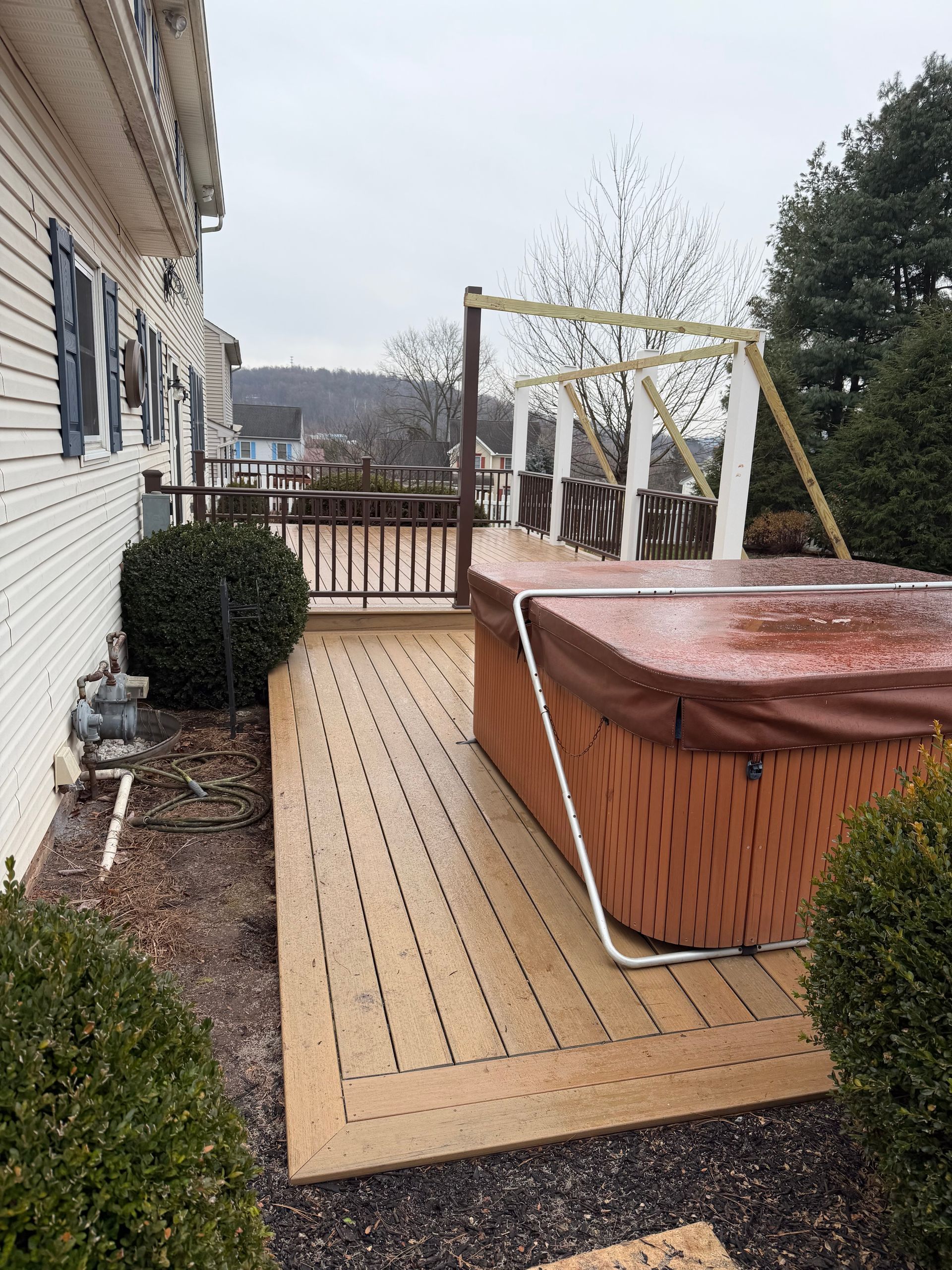 A light-brown deck featuring a hot tub with a cover and a partially constructed wooden pergola frame in an outdoor yard.
