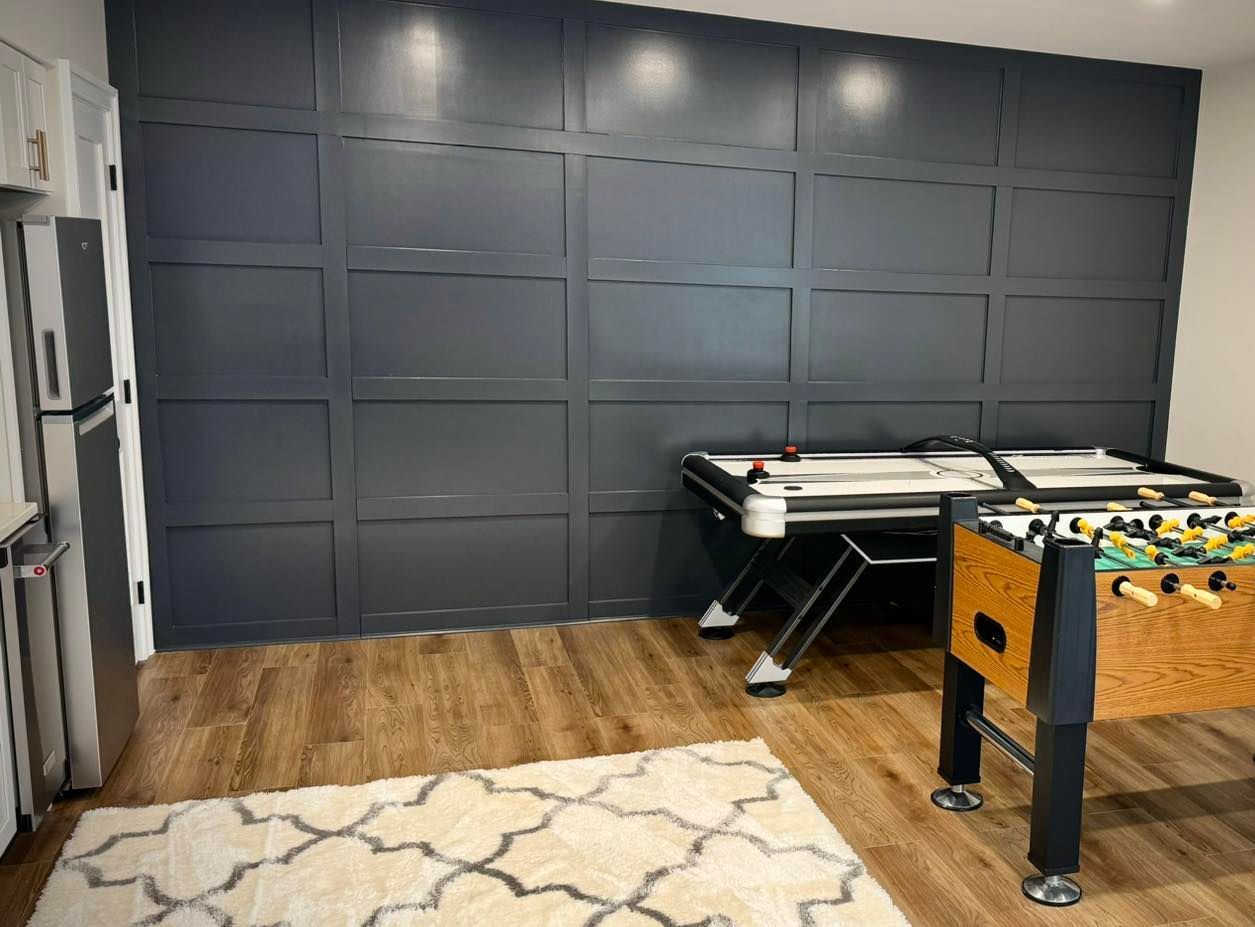 A game room featuring a dark gray paneled accent wall, a foosball table, an air hockey table, and a patterned rug.