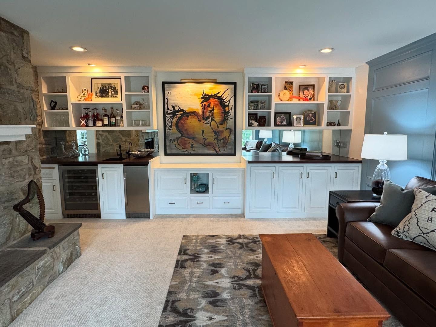A home bar with white built-in cabinets, a wine fridge, open shelving, and a large central painting of a horse.