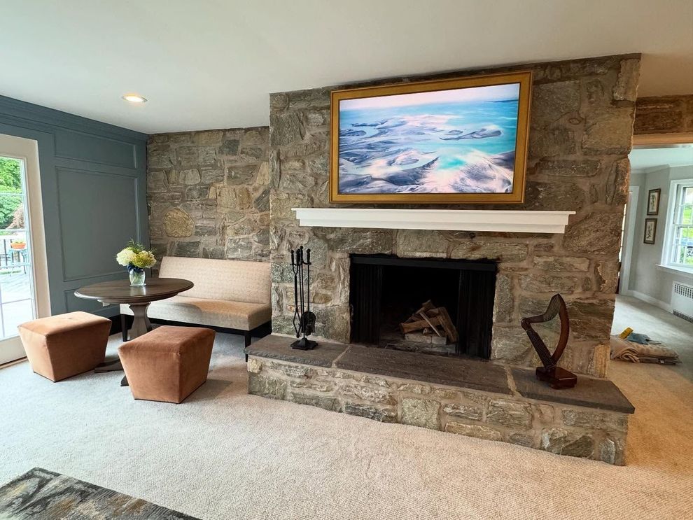Stone fireplace with a mounted television above a white mantel, beside a small table with chairs in a carpeted room.