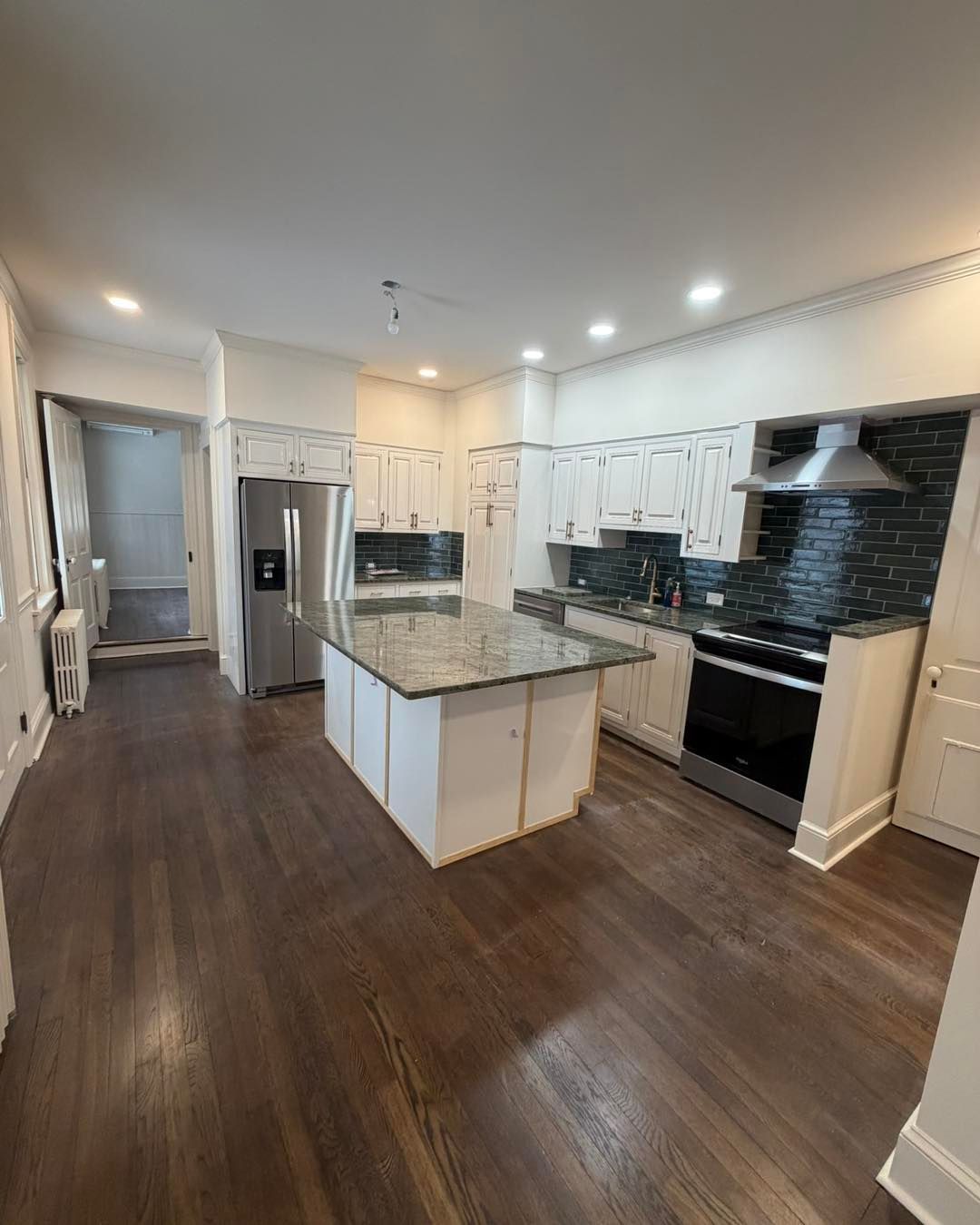 Modern kitchen with white cabinets, dark granite island, stainless steel appliances, and dark hardwood floors.