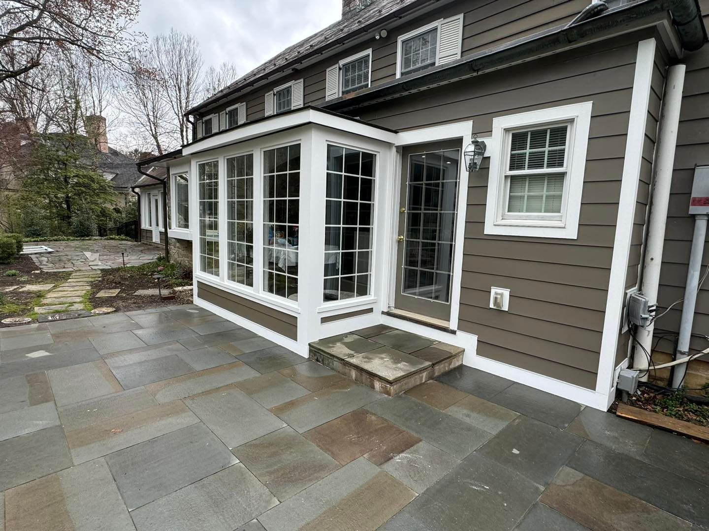 A sunroom extension with large windows and a glass door, attached to a house with brown siding and a stone patio.