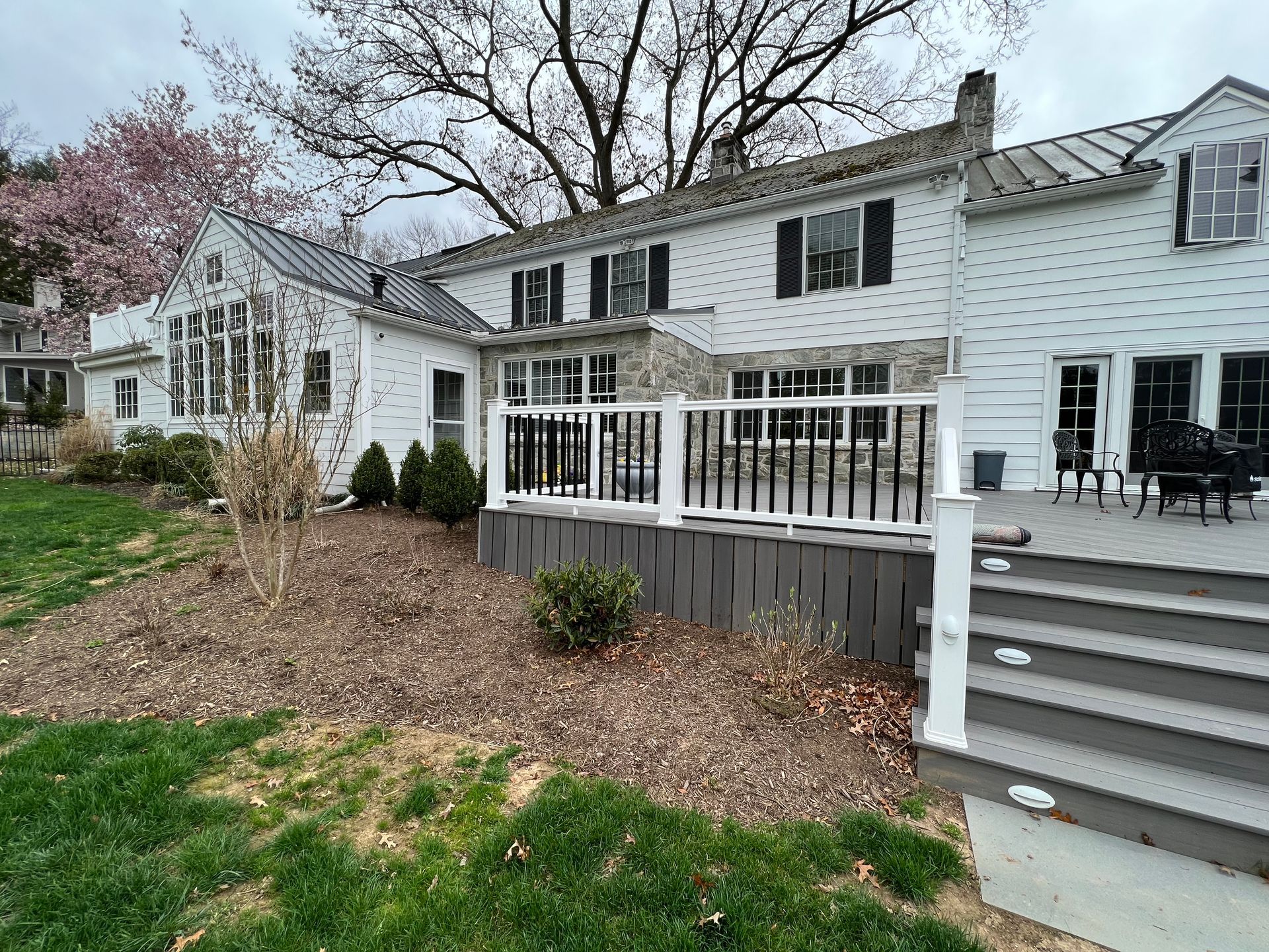 A white, two-story house with a grey deck, stairs from the backyard on a cloudy day in Lancaster, PA.