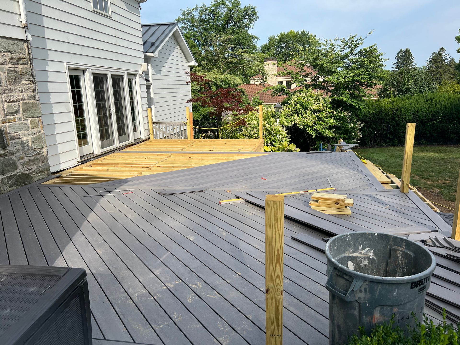 A partially constructed deck with gray composite boards and natural wood support posts outside a white house.