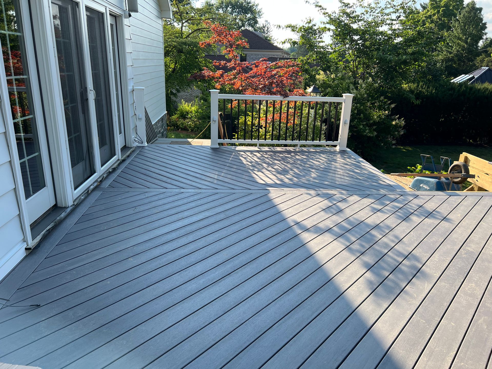 A spacious gray wooden deck featuring a surrounding railing, viewed from an elevated angle next to a stone building wall.