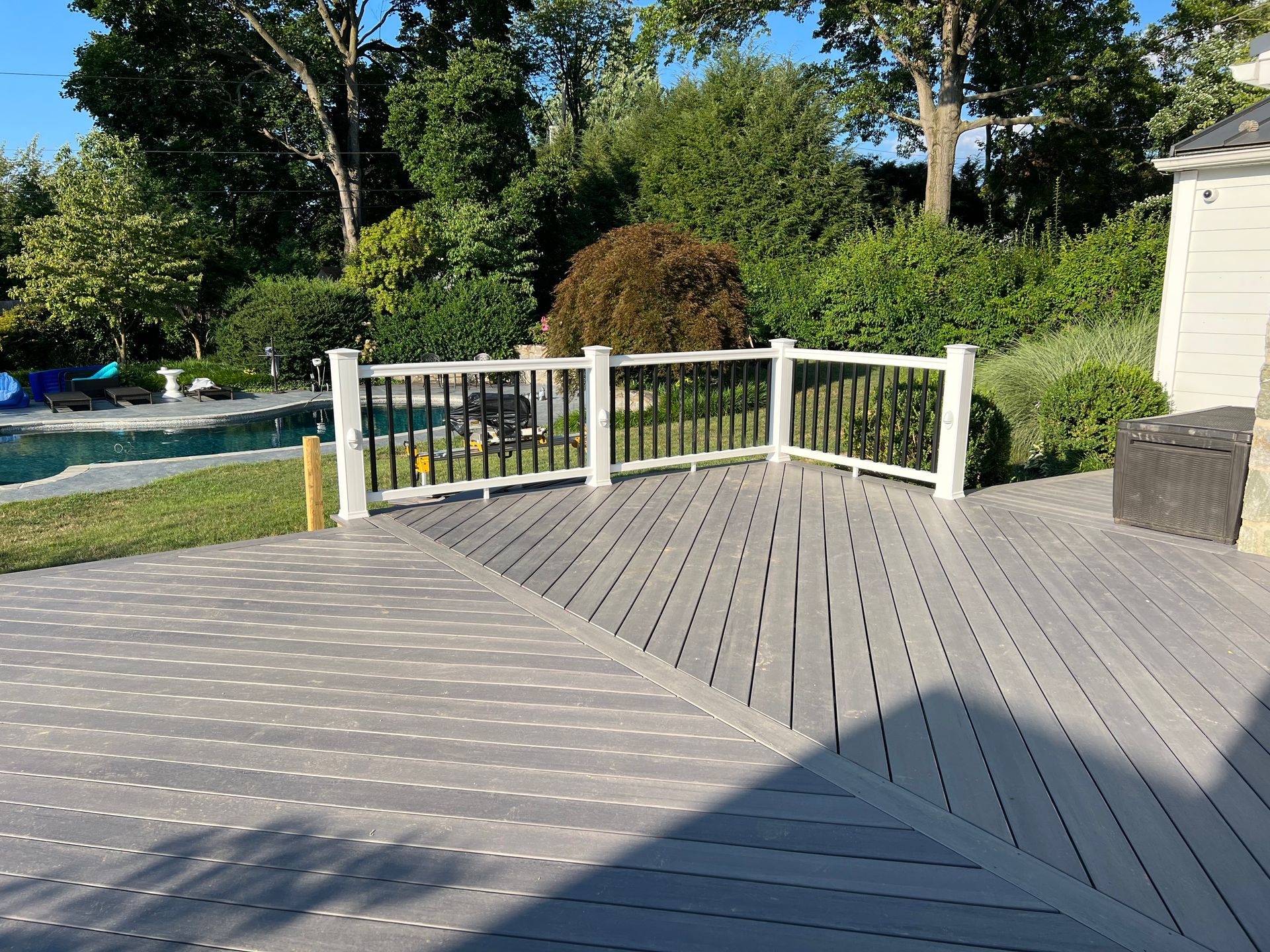 A gray composite deck with black railings overlooks a backyard with a swimming pool and lush green trees.