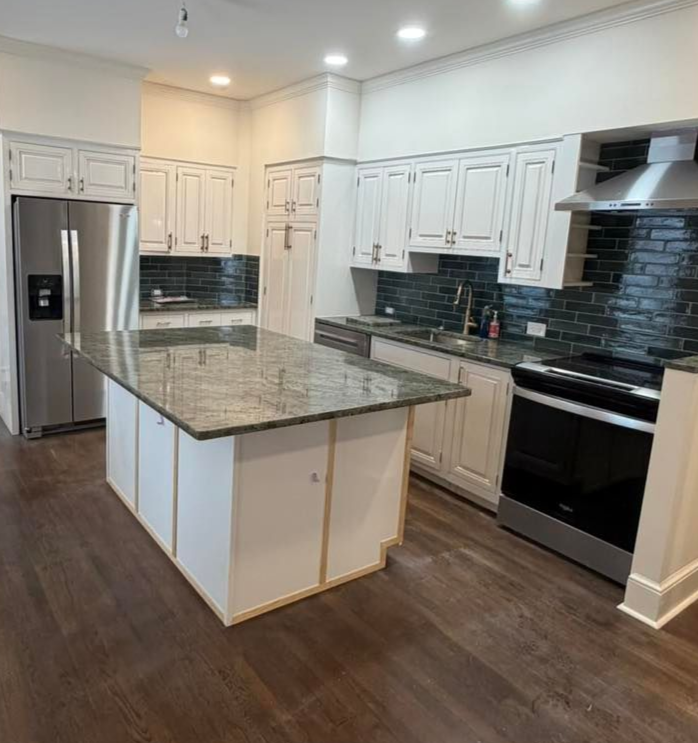 A modern kitchen featuring white cabinets, dark granite countertops, a central island, and black brick backsplash.
