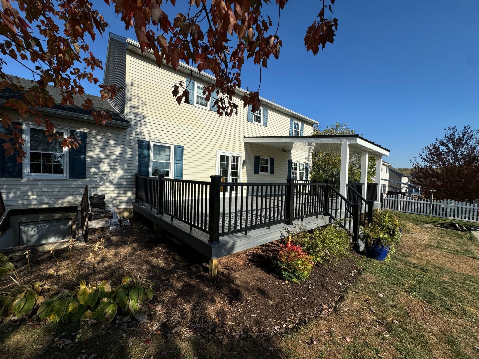 A white two-story house with a grey deck, wooden stairs, and a mulch garden bed on a cloudy day.